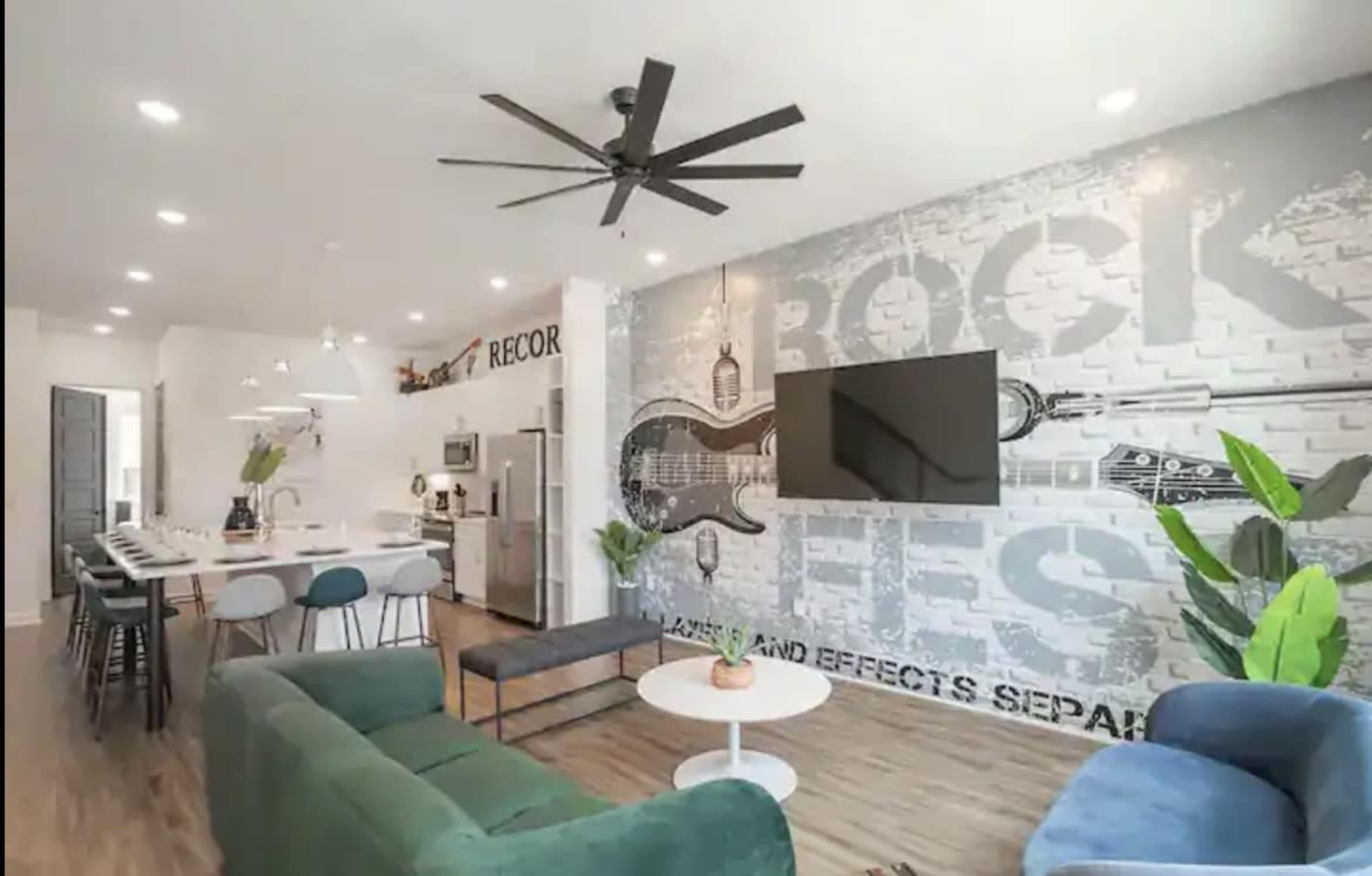 A modern, open-concept living space with a dark gray accent wall featuring large musical-themed graphics, a seating area with a blue couch and green chairs, and a dining area visible in the background.
