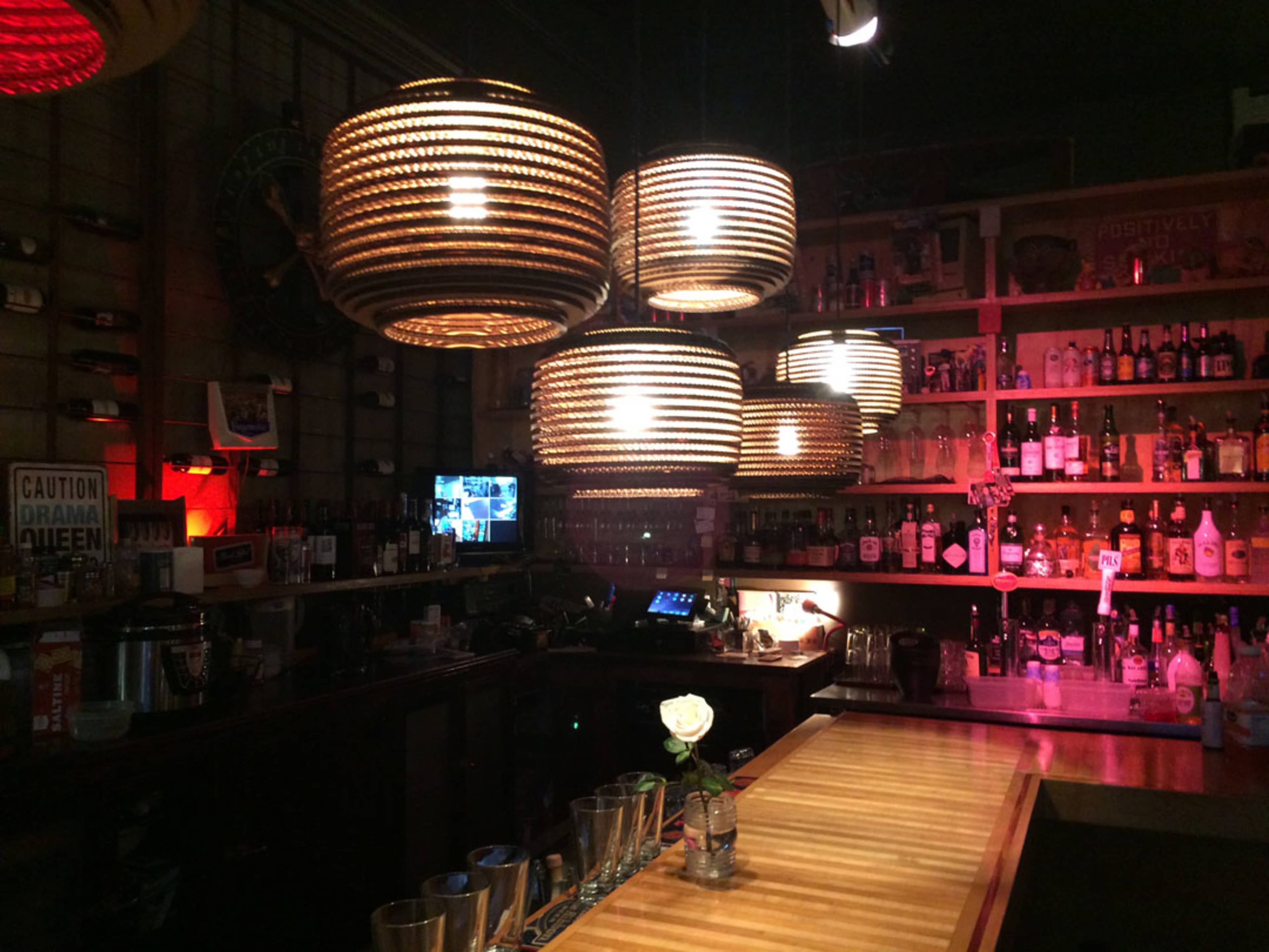 A dimly lit bar with wooden countertops, round pendant lights, and shelves stocked with various bottles.
