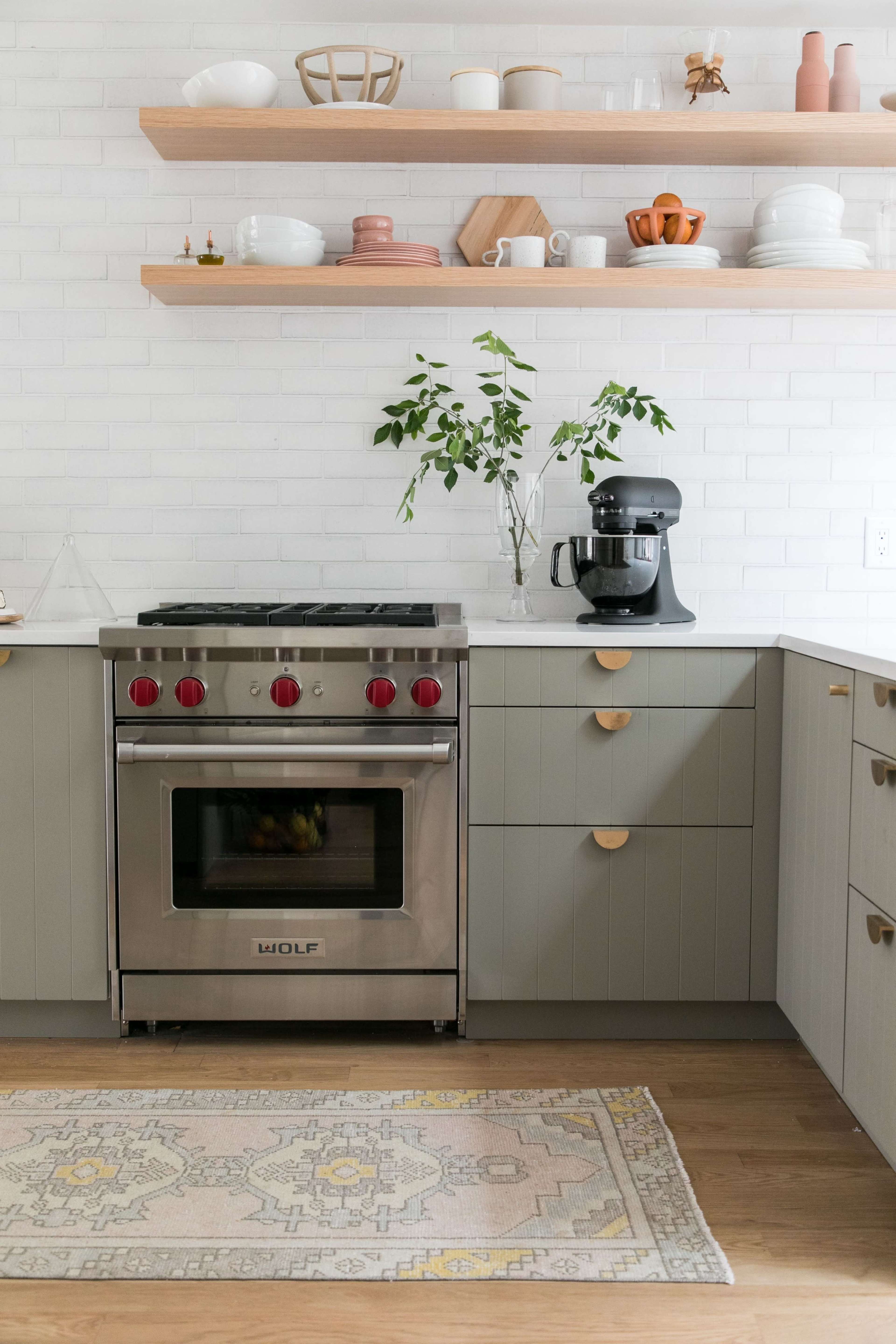 A modern kitchen features a stainless steel range, light-colored cabinetry, and open shelves displaying various kitchenware.