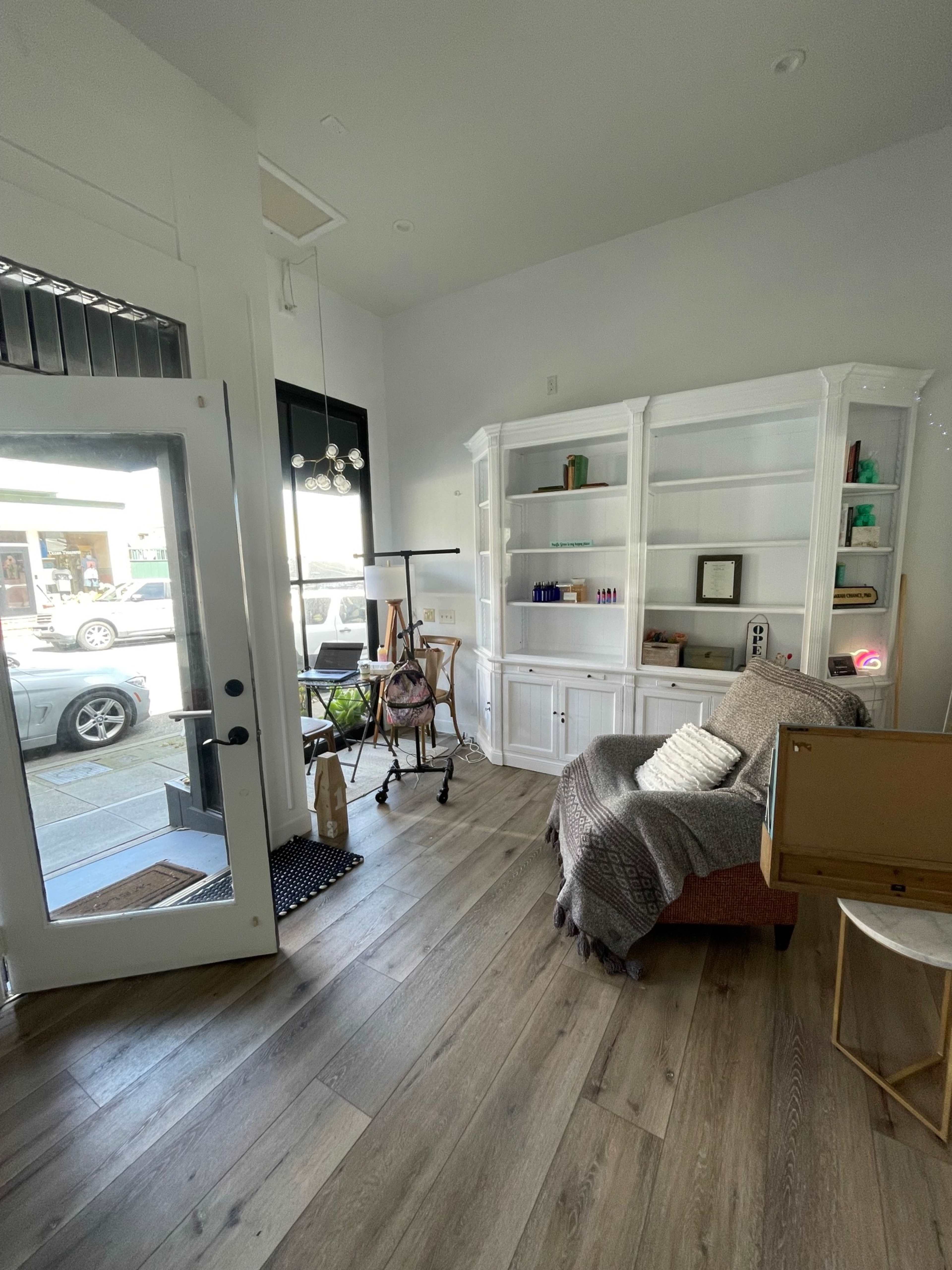 A well-lit room with a white bookshelf, a sofa, and a large window facing the street.