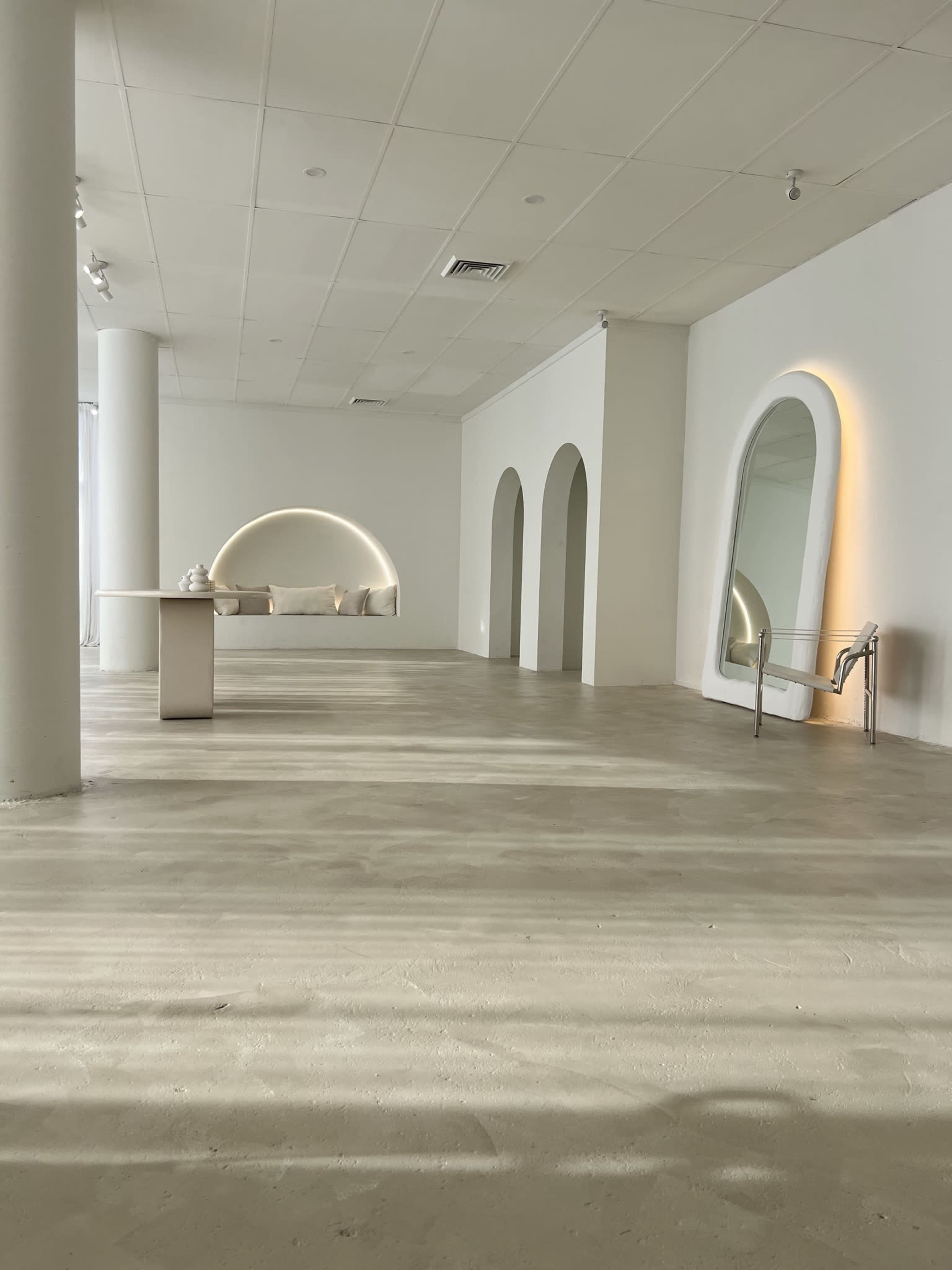 A spacious, minimalist room with white walls, arched openings, and a small table along one side.