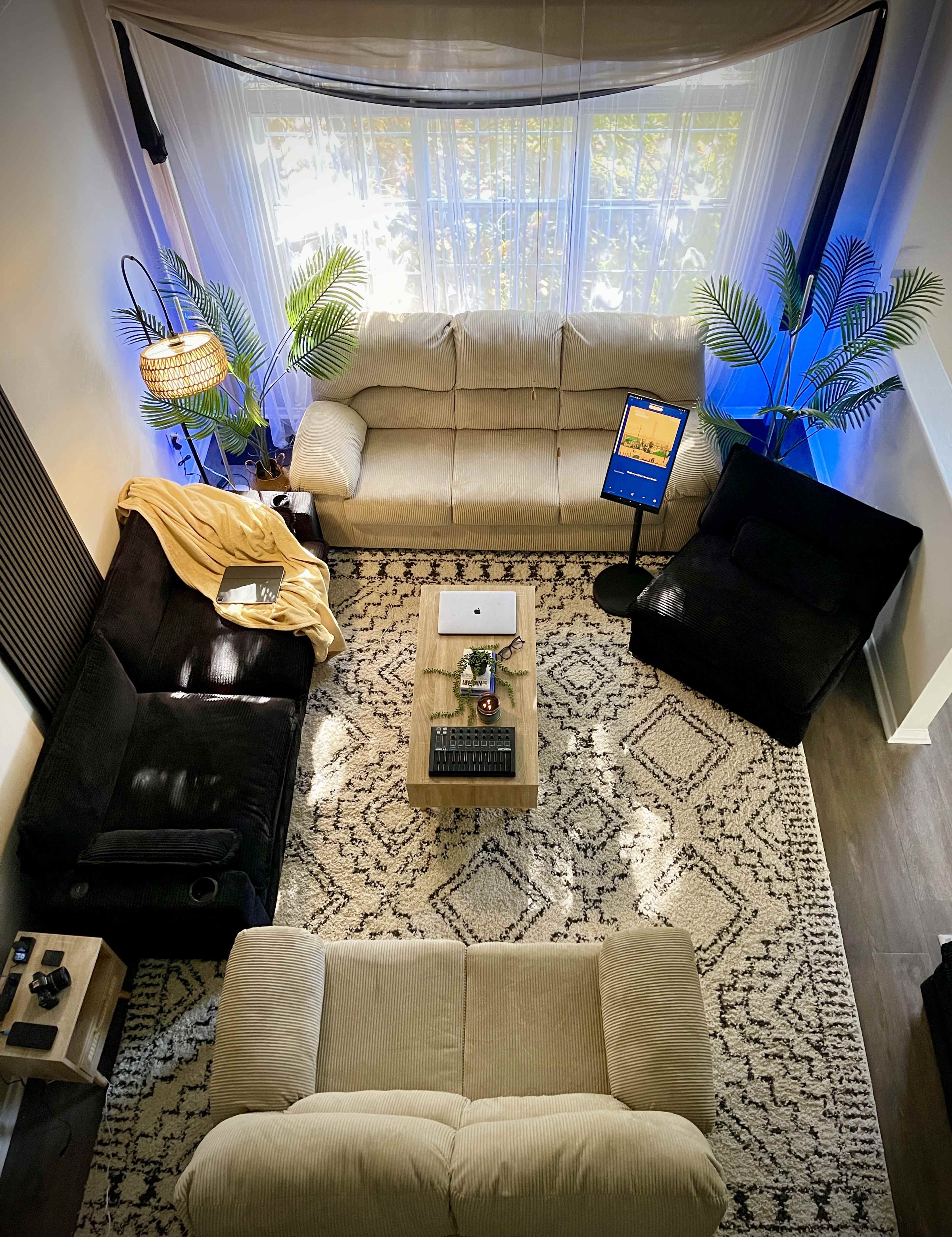 The image shows a modern living room with two sofas, a coffee table, a laptop, and decorative plants under soft lighting.