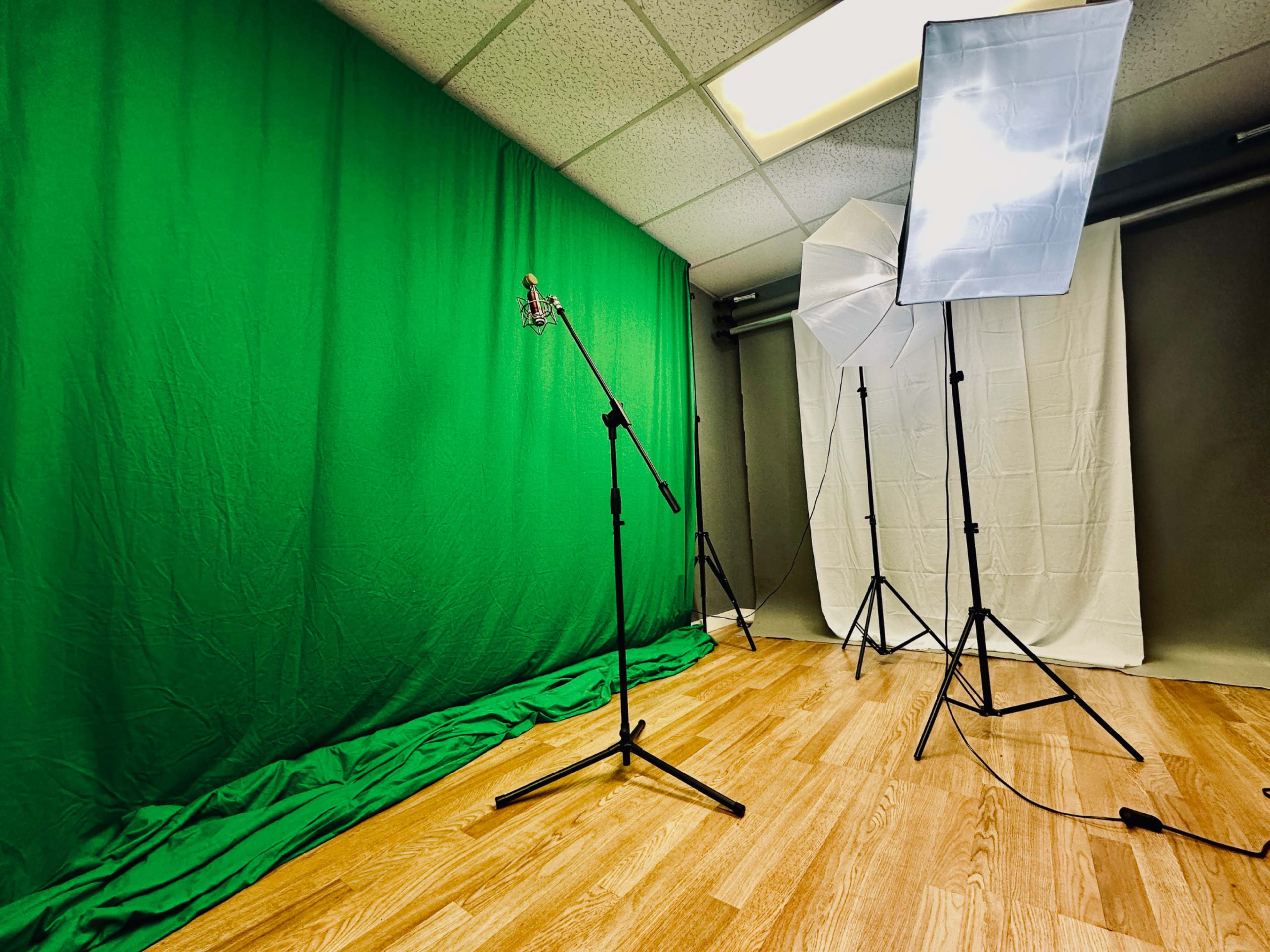 A green screen setup with a microphone on a stand and two light stands in a studio environment.