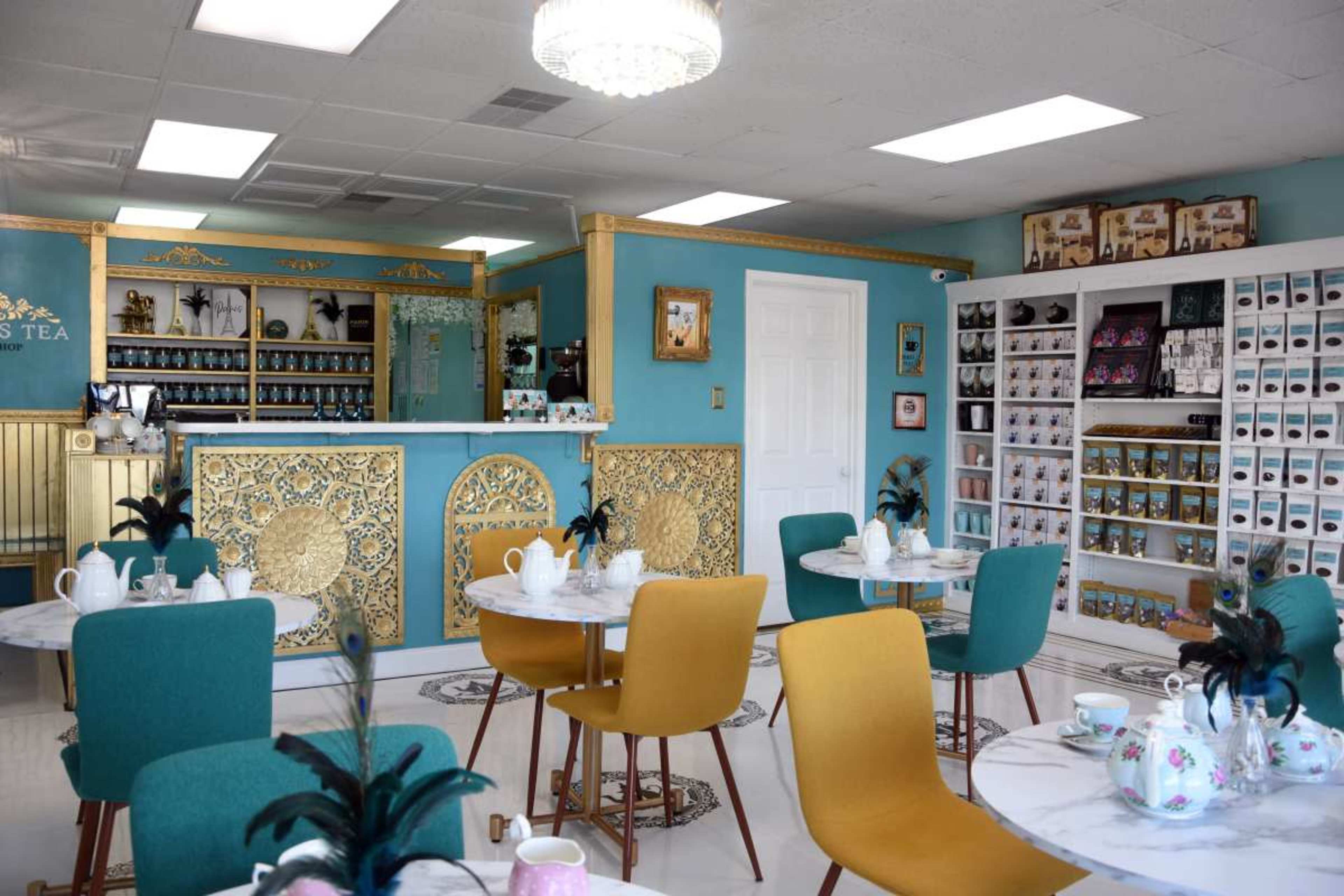 A brightly lit tea shop with elegantly designed tables and a display of various tea products on shelves.