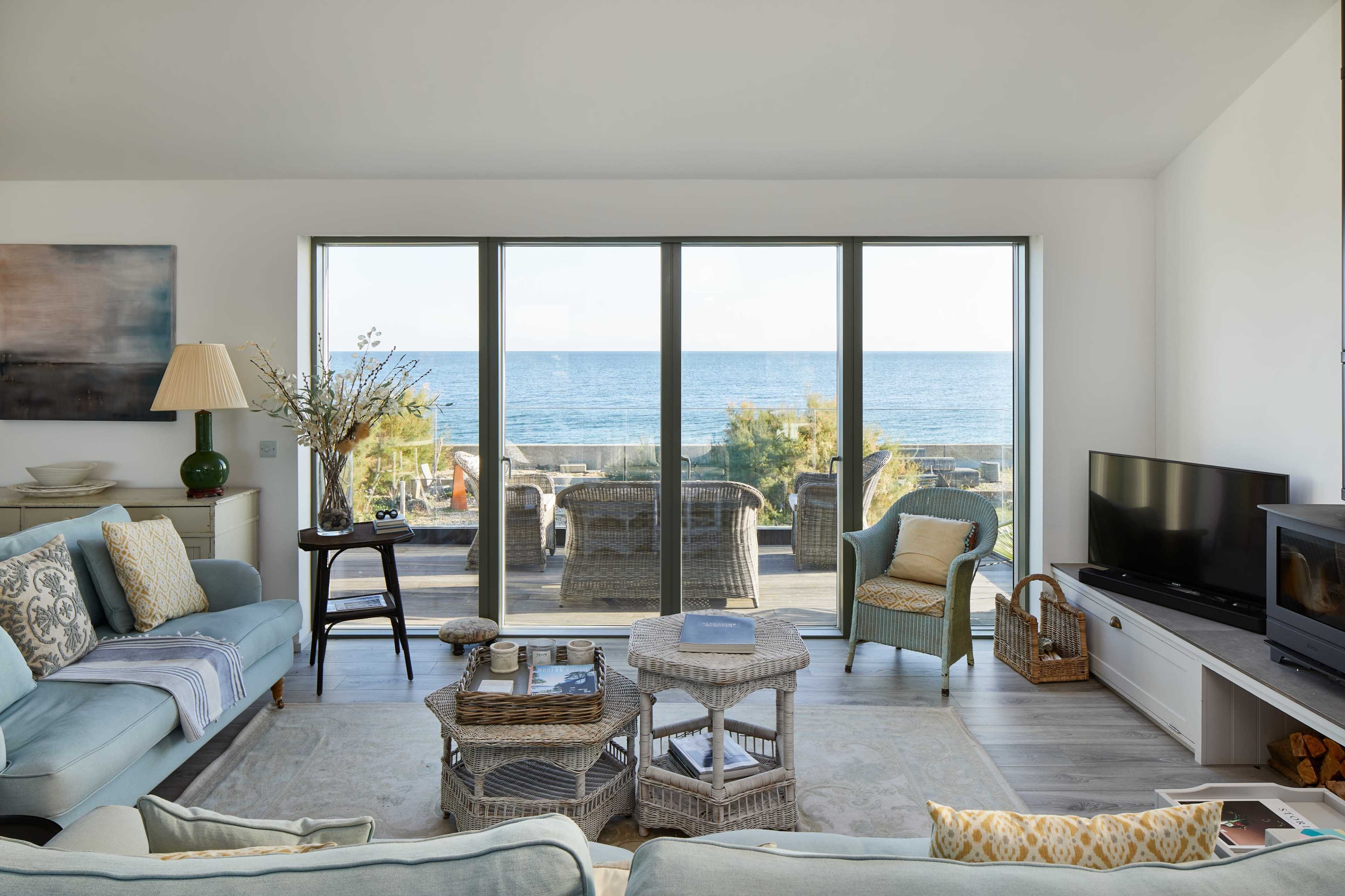 A modern living room features light-colored furniture and large glass doors that open to a view of the ocean.