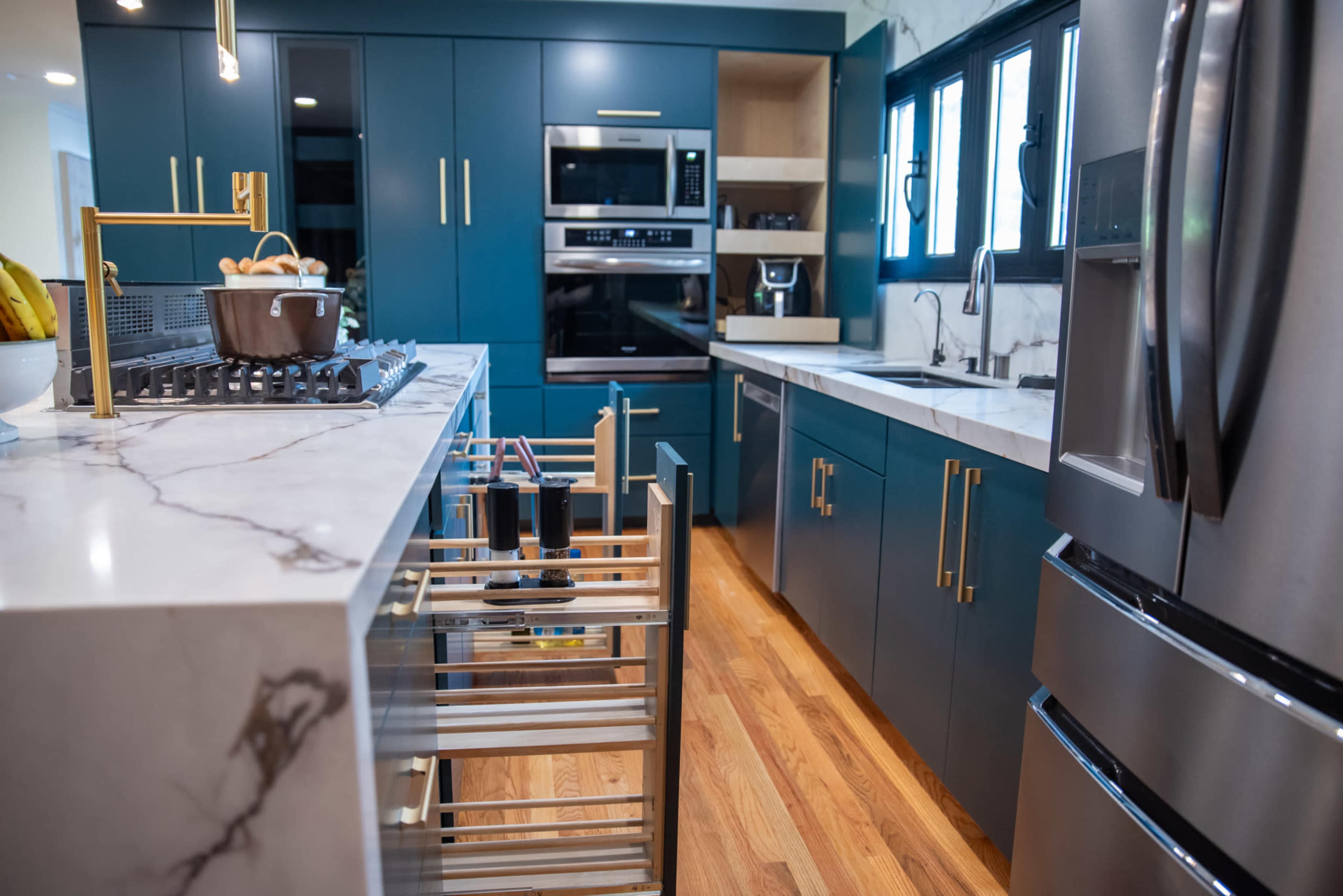 The image shows a modern kitchen featuring navy blue cabinetry, stainless steel appliances, and a marble countertop.
