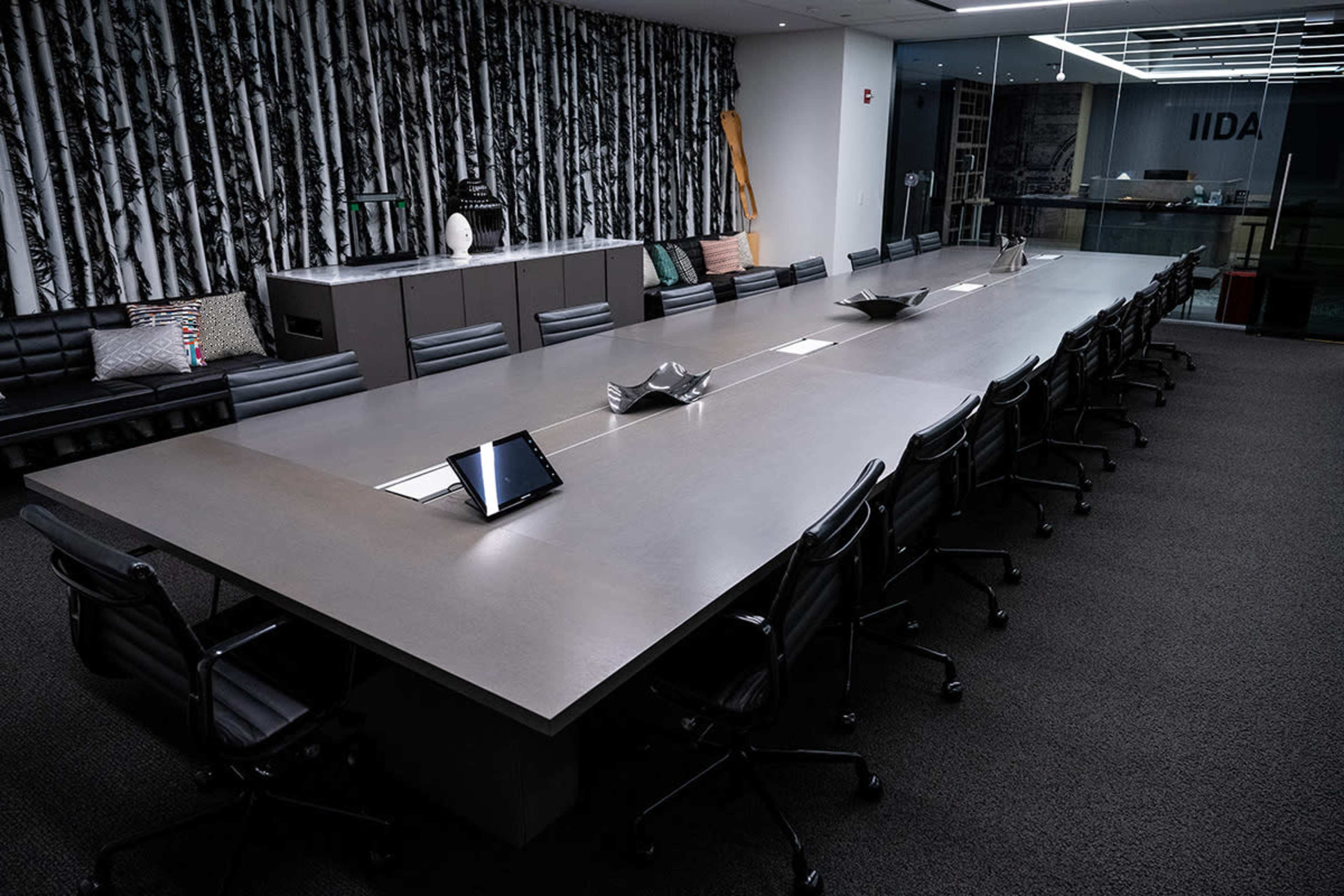 A long, rectangular conference table is positioned in a modern meeting room with a patterned wall and various seating arrangements.
