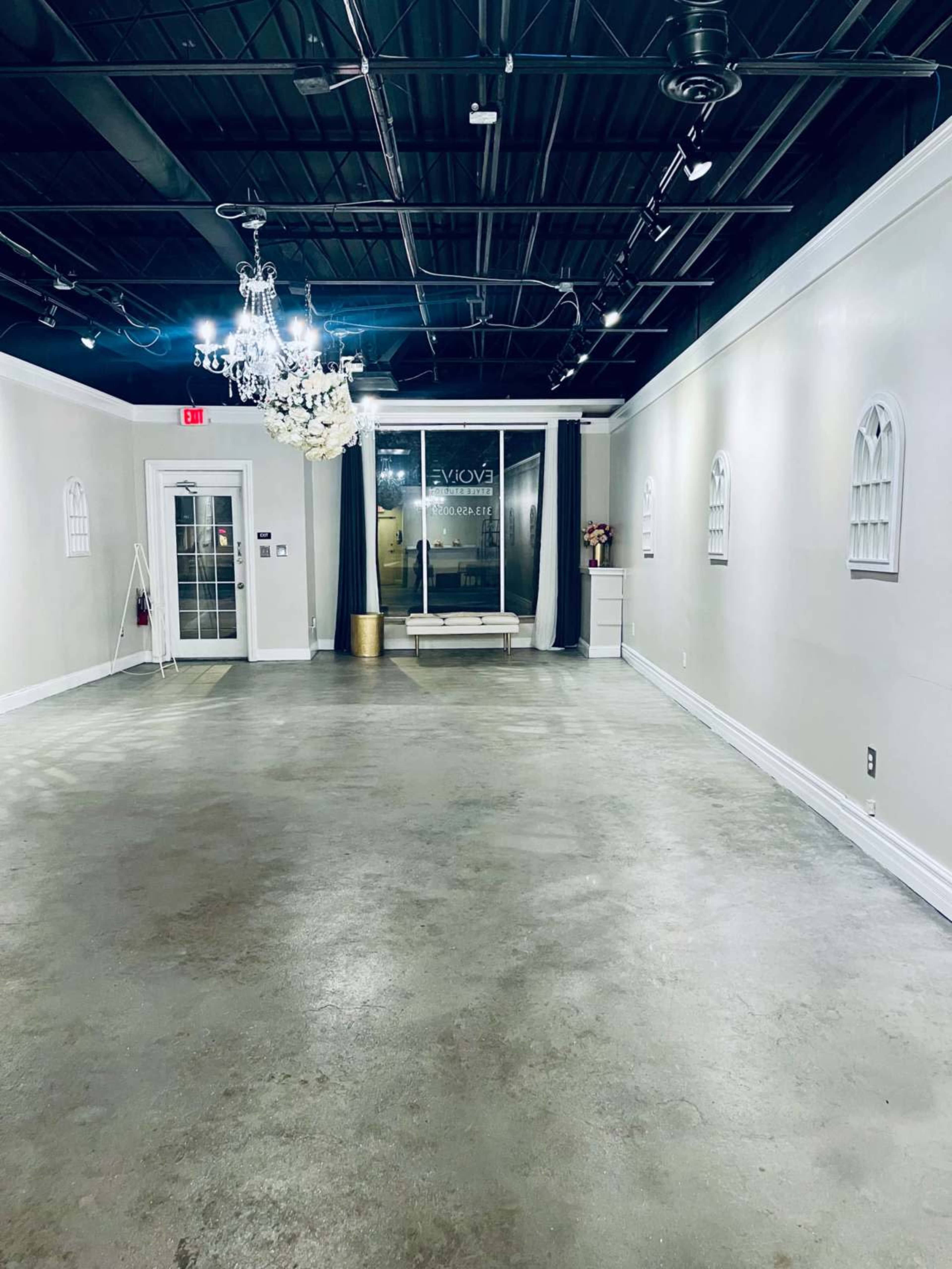 The image shows an empty, well-lit interior space with a concrete floor, white walls, and a chandelier hanging from the ceiling.