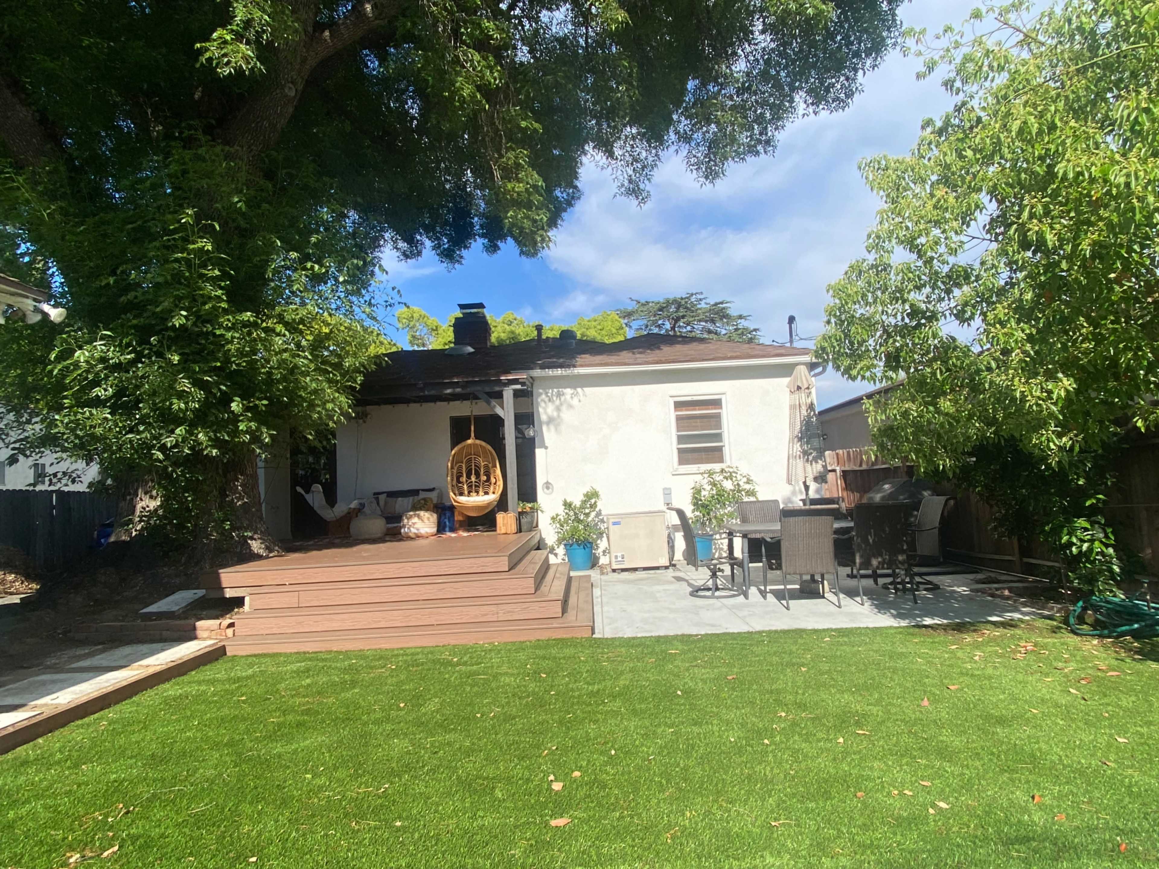 The image shows a backyard with a green lawn, a wooden deck, outdoor furniture, and a house with a chimney.