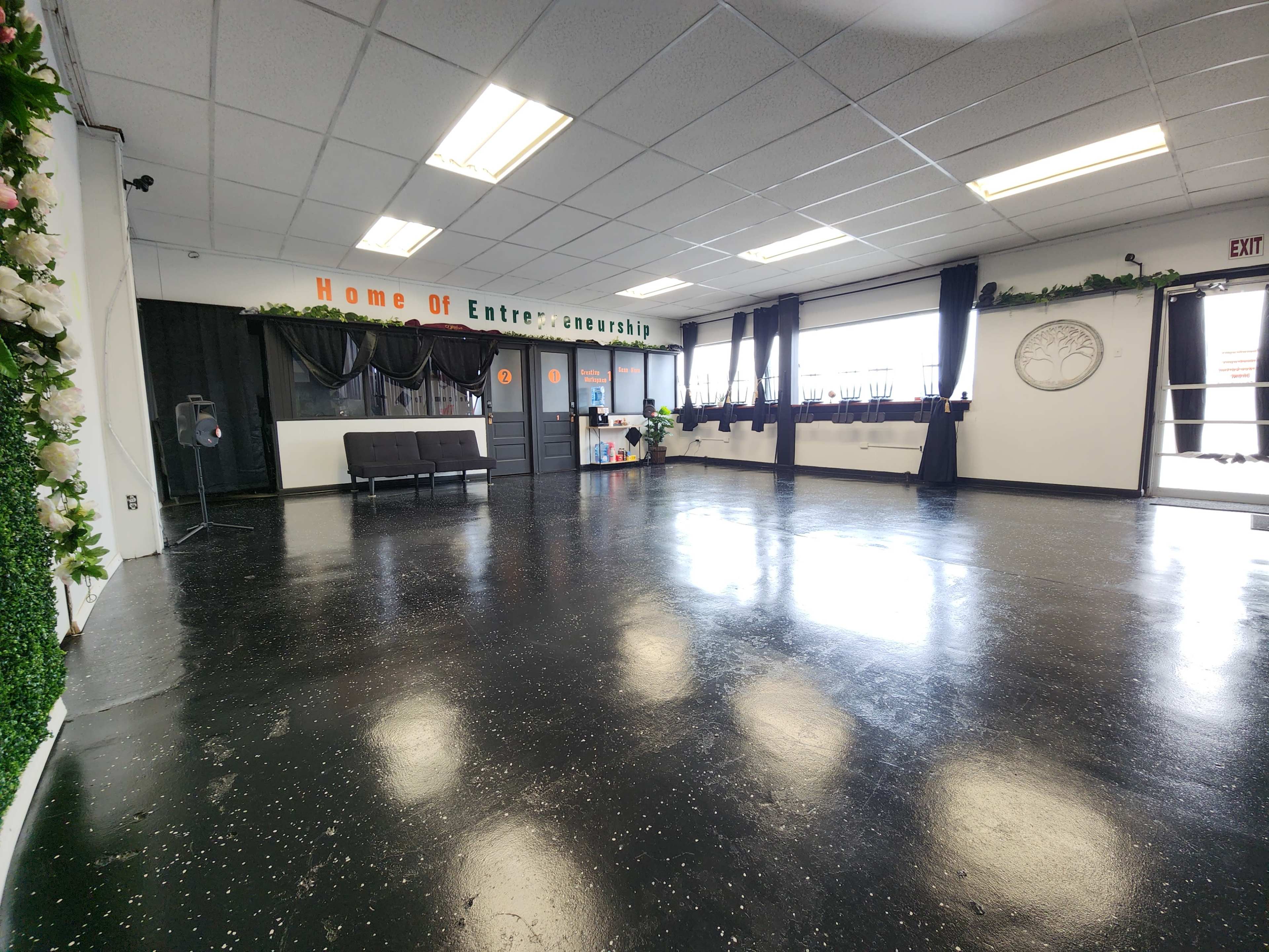 The room features a spacious, empty floor with black glossy tiles and is decorated with a floral wall on one side, a bench, and large windows.