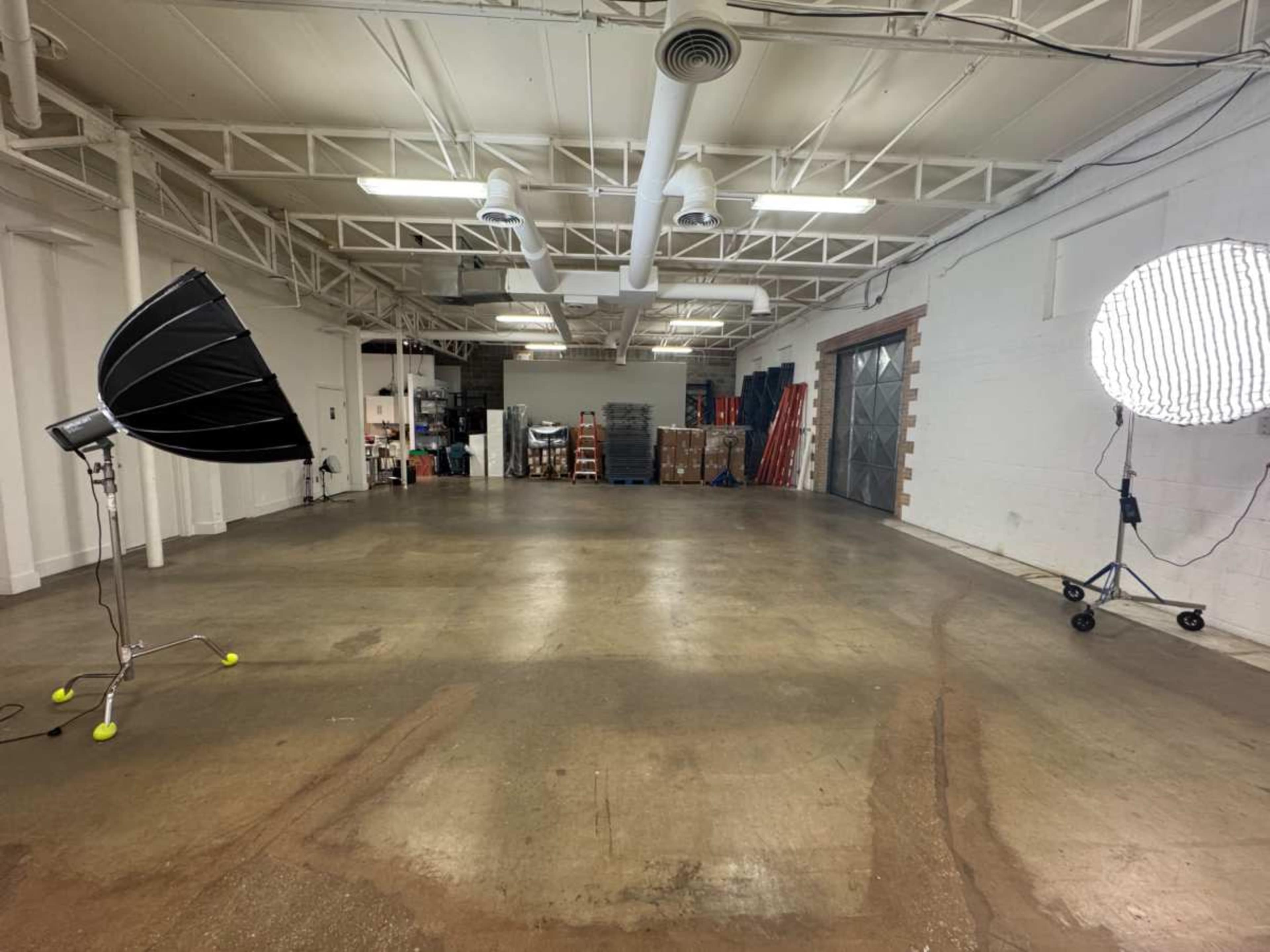 The image shows an empty industrial space with two large lights positioned to the left and right, and stacks of equipment stored against the back wall.