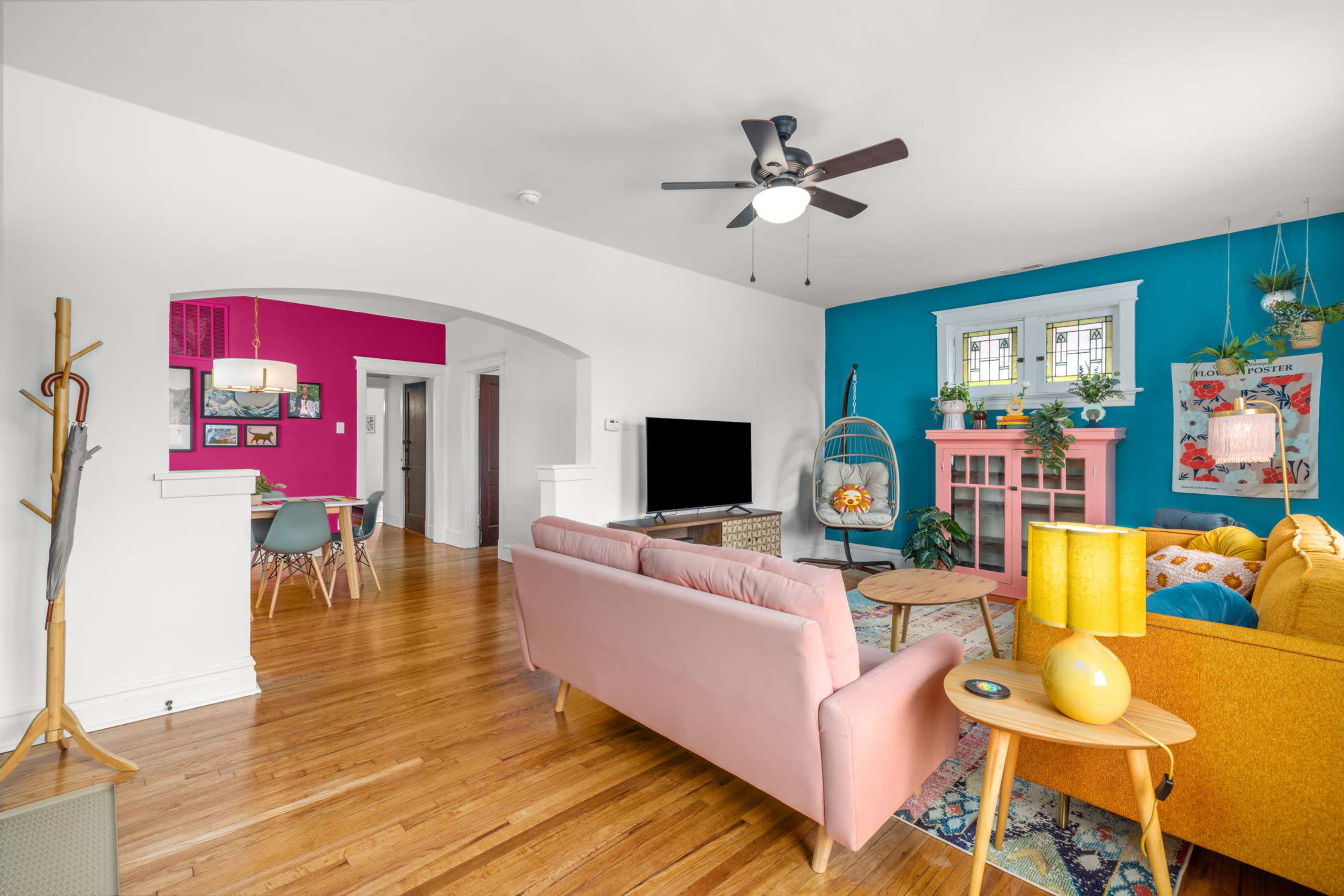 The living room features a mix of colorful furniture, including a pink sofa and yellow armchair, paired with hardwood floors and a vibrant blue accent wall.