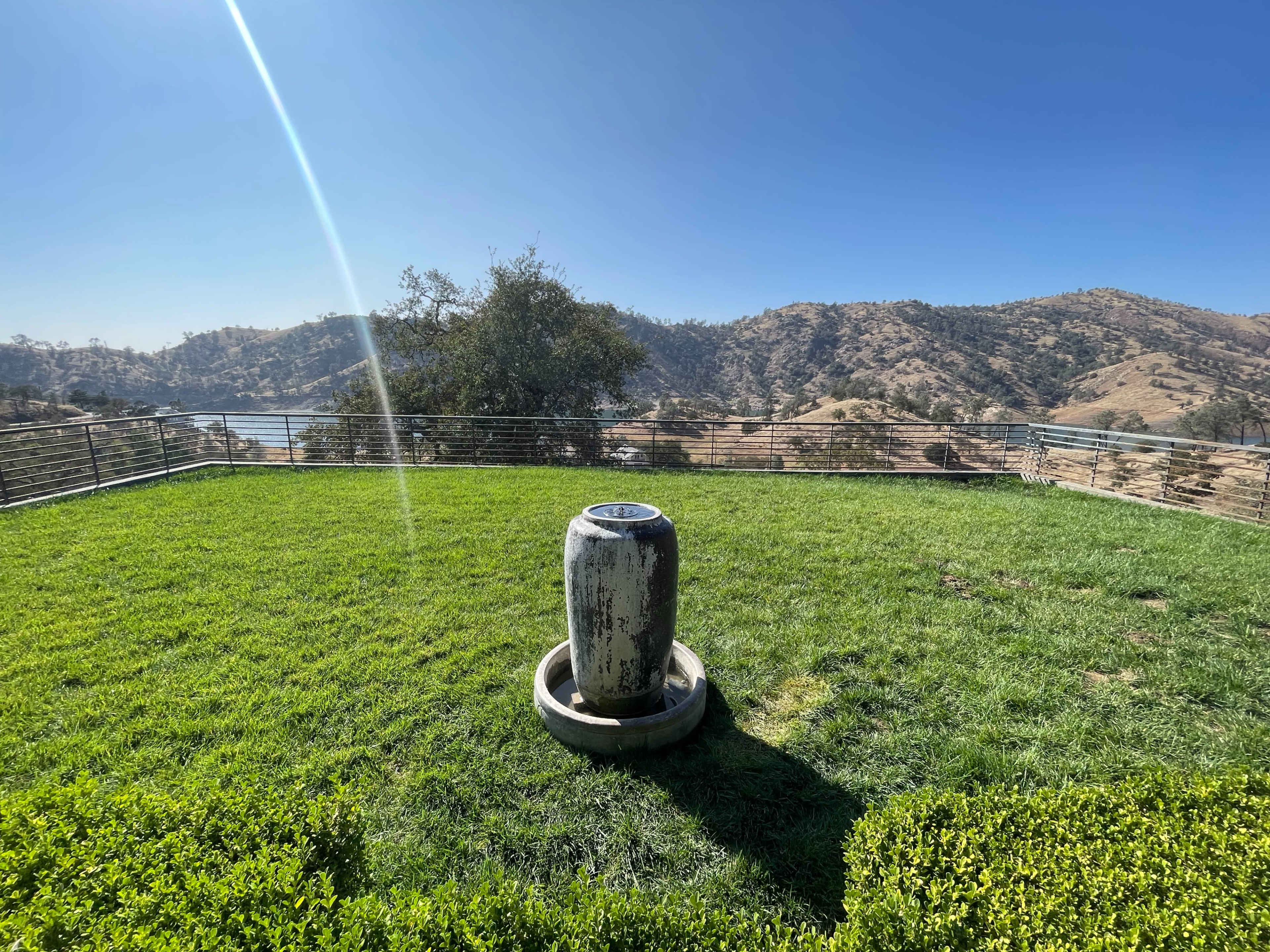 A stone water feature stands on a green hillside overlooking a lake and rolling mountains in the distance.