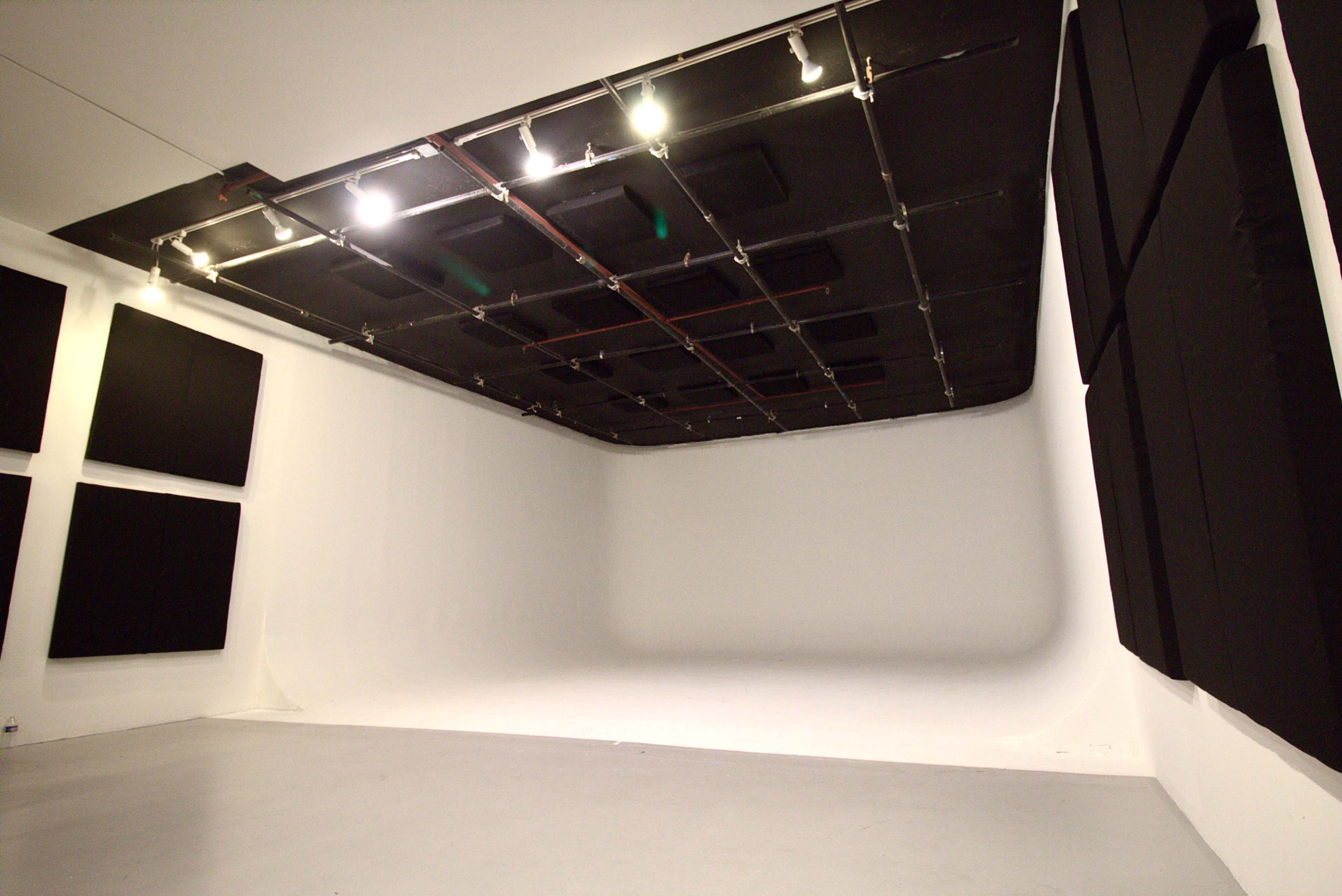 The image shows a spacious, empty studio with a white backdrop and black sound-absorbing panels on the walls.