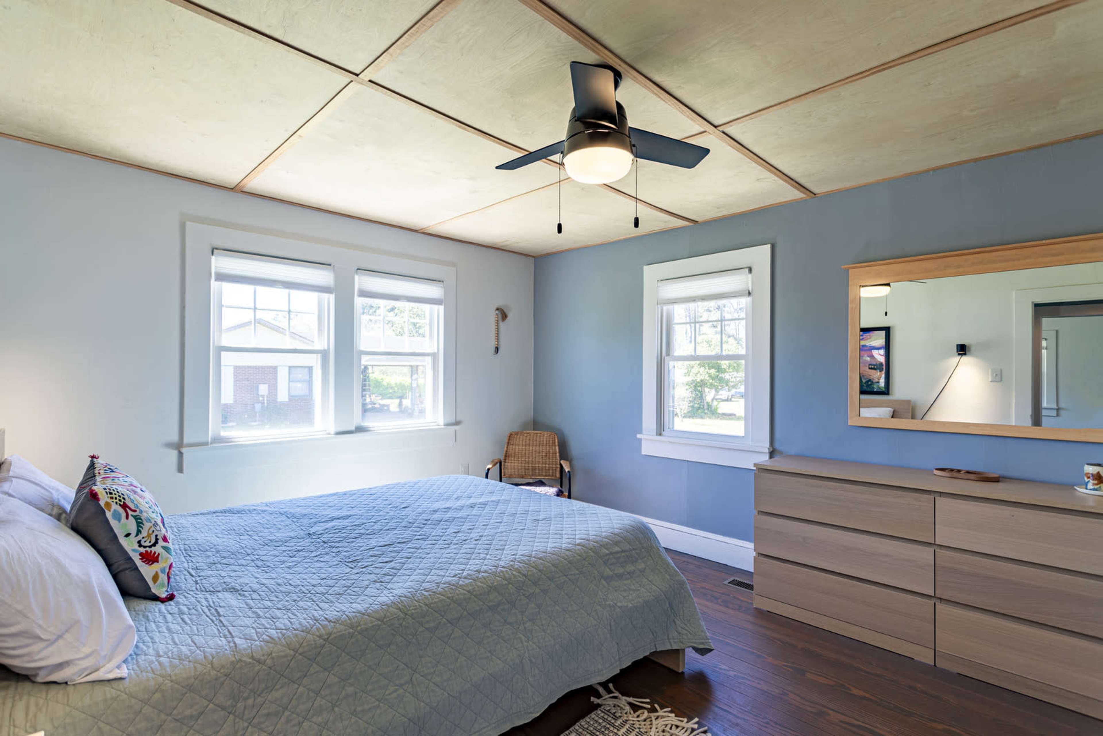 The room features a bed with a quilt, a dresser, a ceiling fan, and windows allowing natural light.