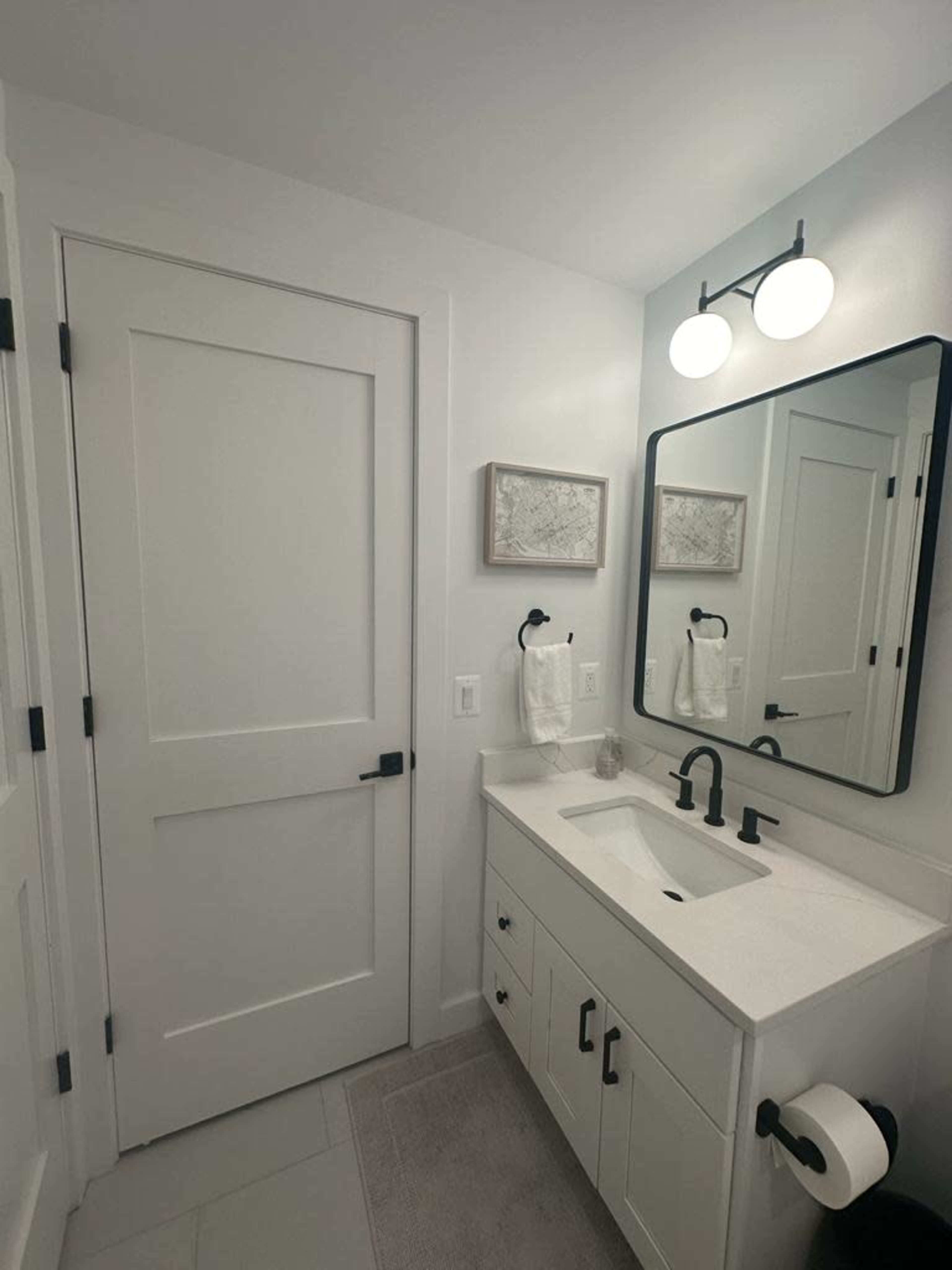 A modern bathroom features a white vanity with a sink, a large mirror, and a door leading to another room.