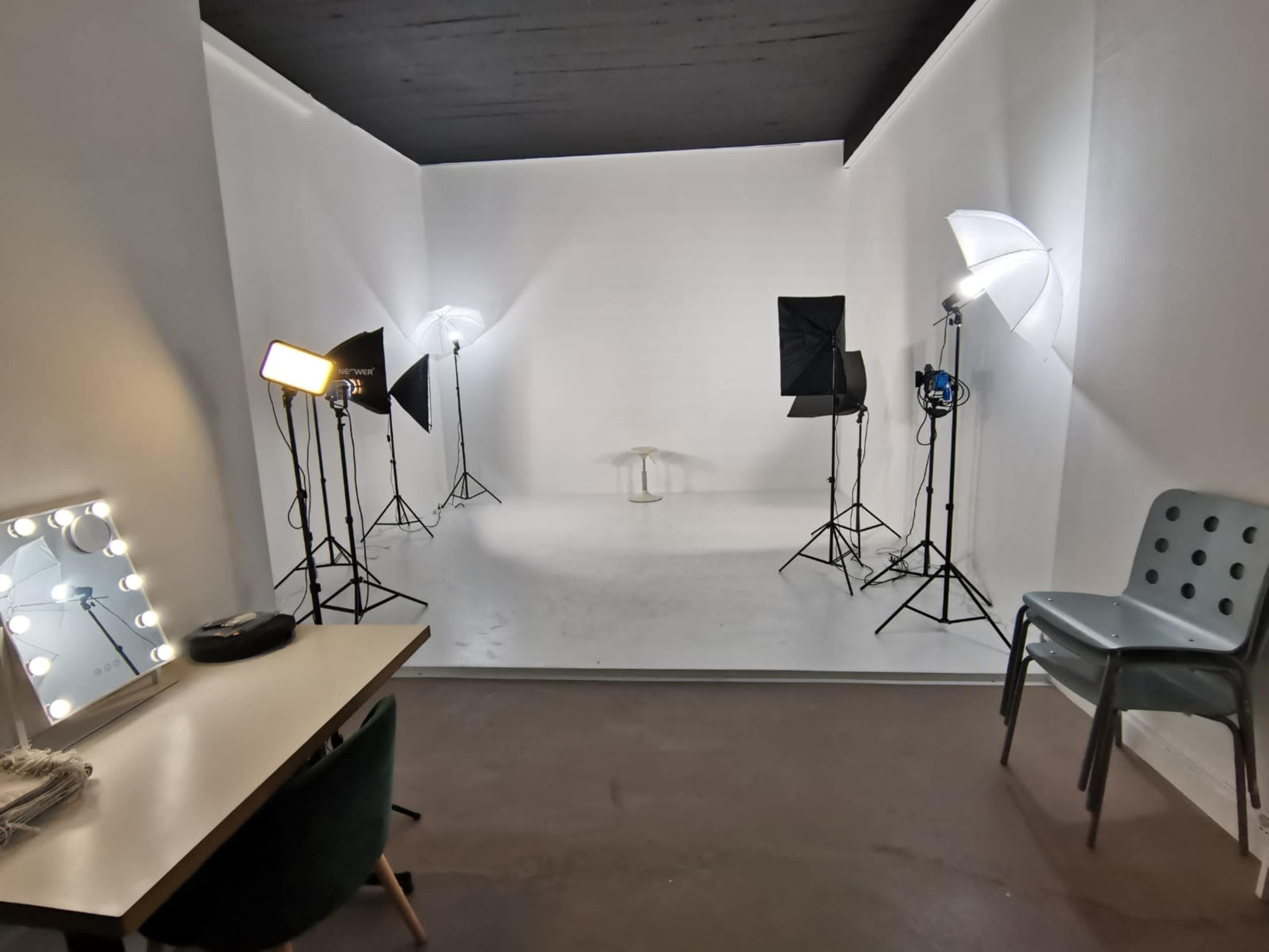 A blank white studio space equipped with lighting setup and a mirrored vanity table in the foreground.