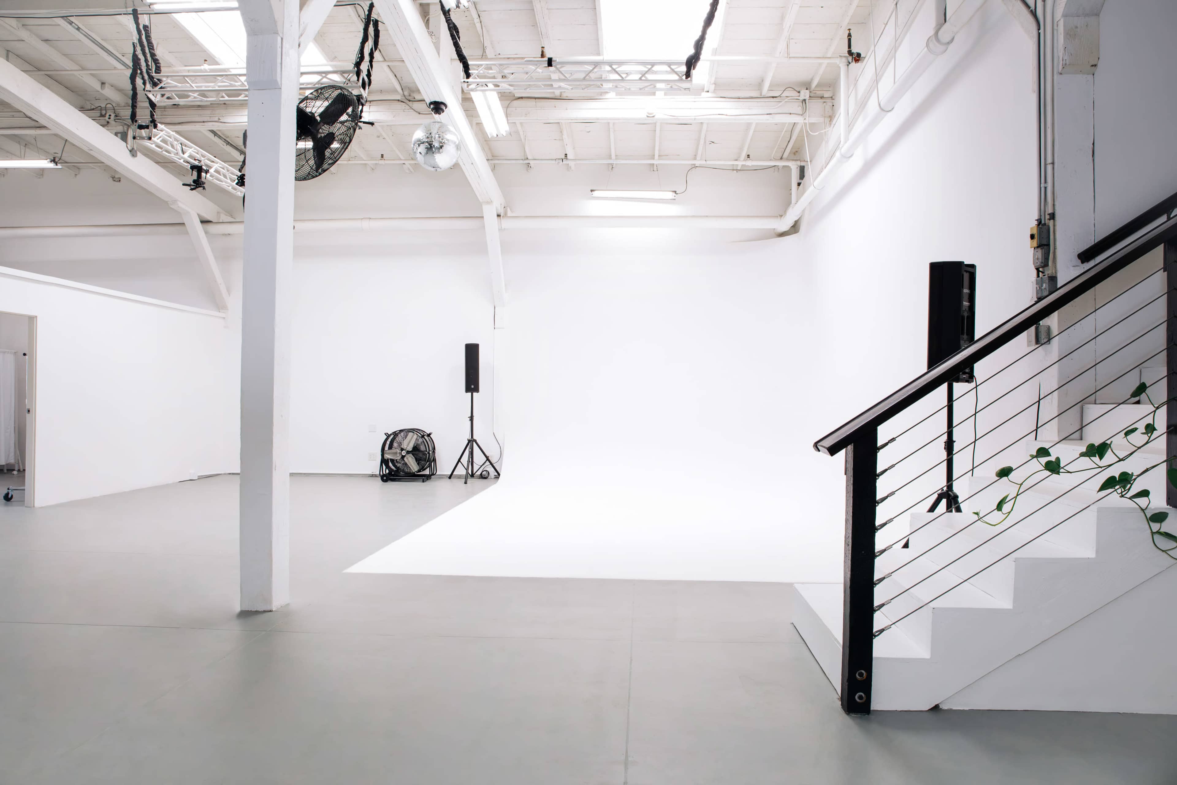 A spacious, well-lit studio with a white backdrop, wooden stairs, and a small fan in the corner.