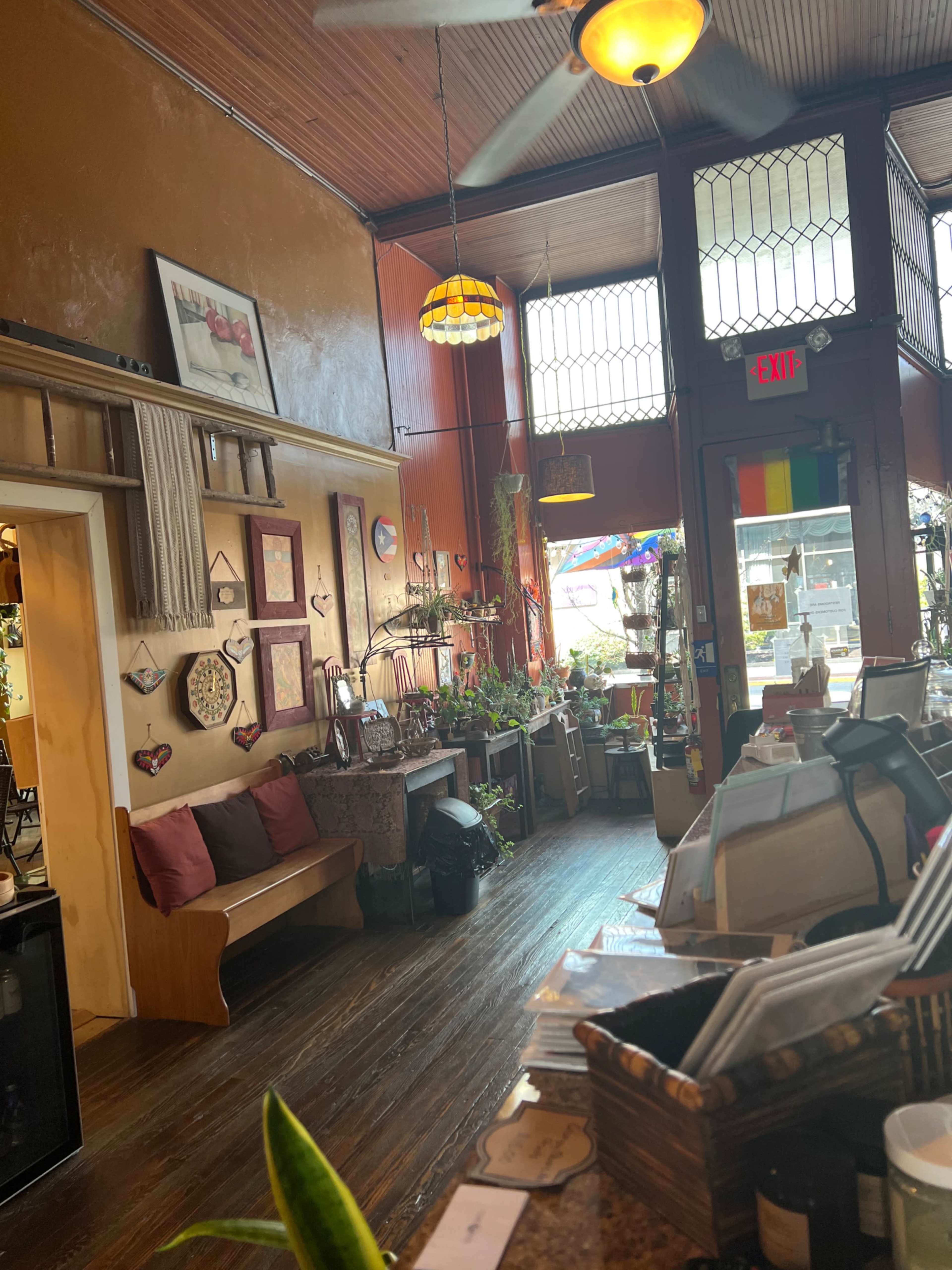 The interior of a cozy cafe with wooden floors, comfortable seating, and decor featuring plants and artwork.