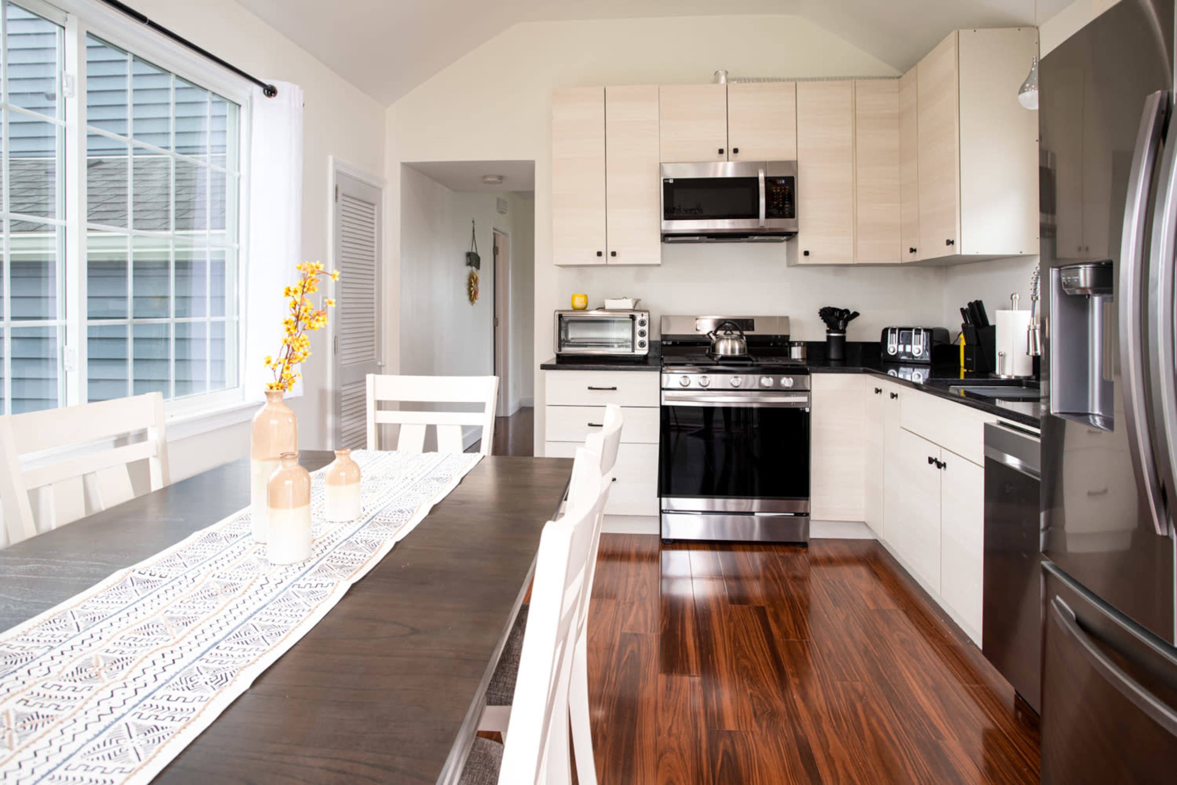 A modern kitchen with light cabinetry, stainless steel appliances, and a dining table set with decorative vases.