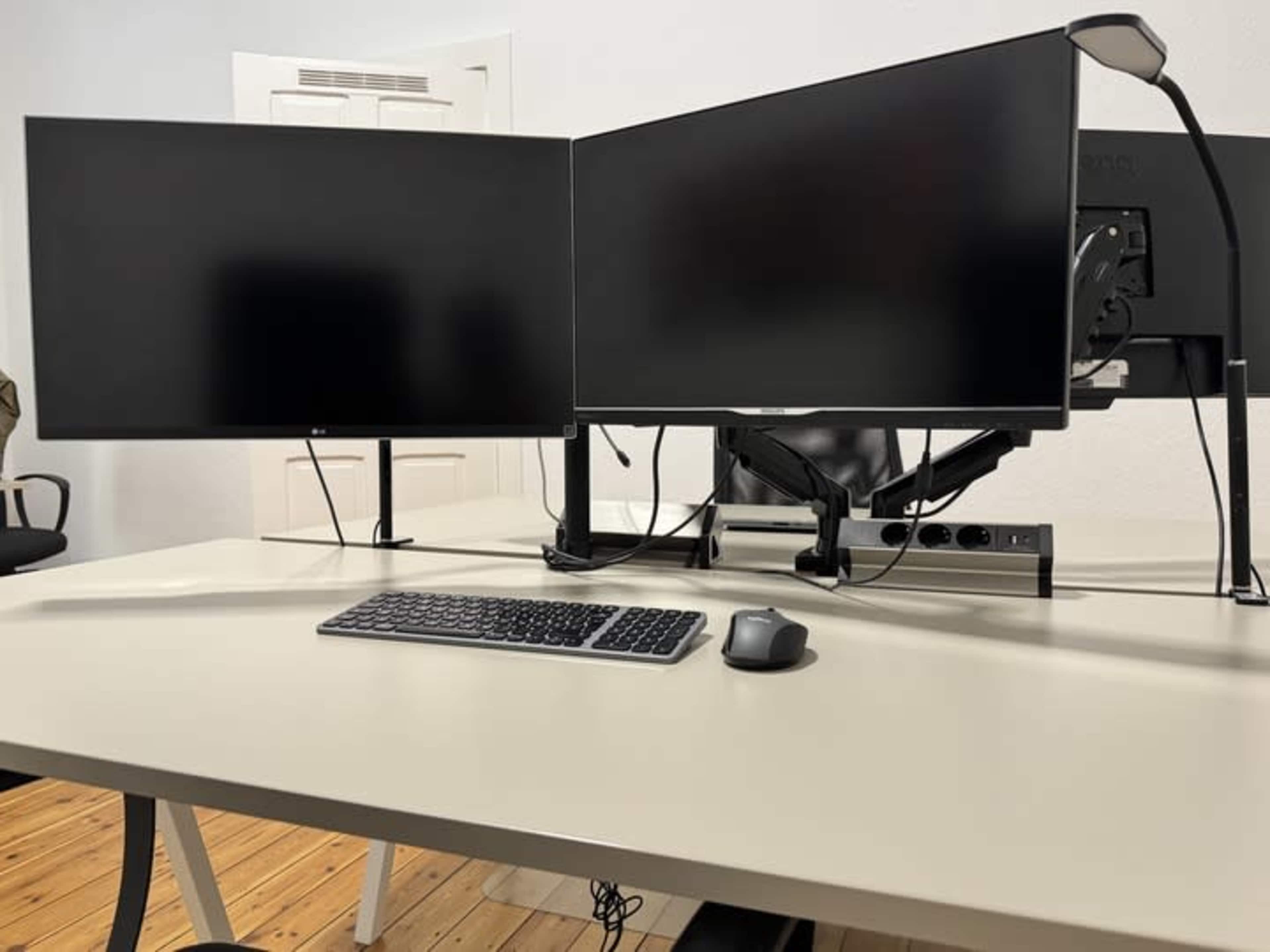 The image shows a workspace with a slim desk and two mounted computer monitors, along with a keyboard and mouse.