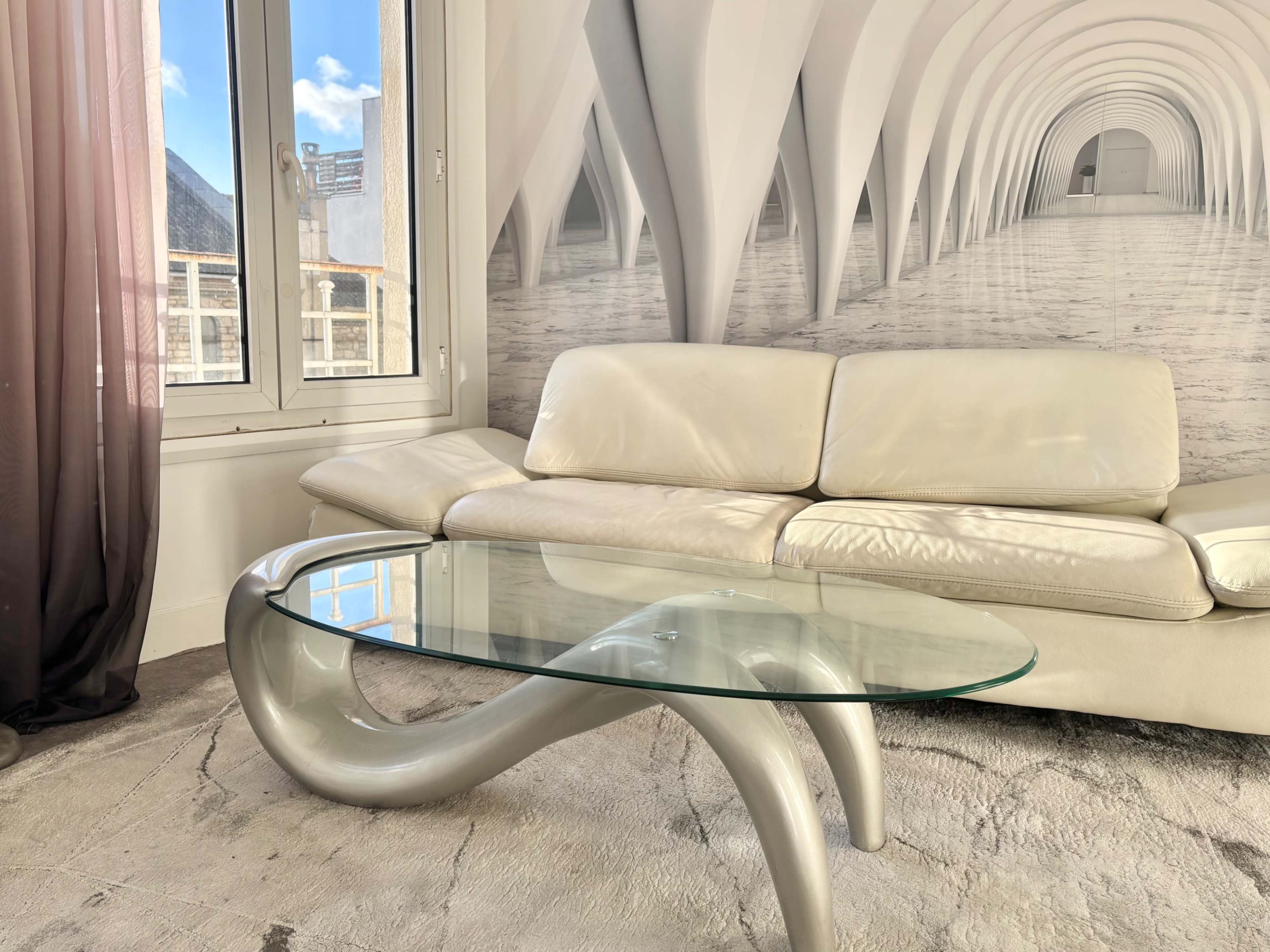 The image shows a modern living room with a white leather sofa and a glass coffee table, set against a backdrop of an architecturally designed wall.