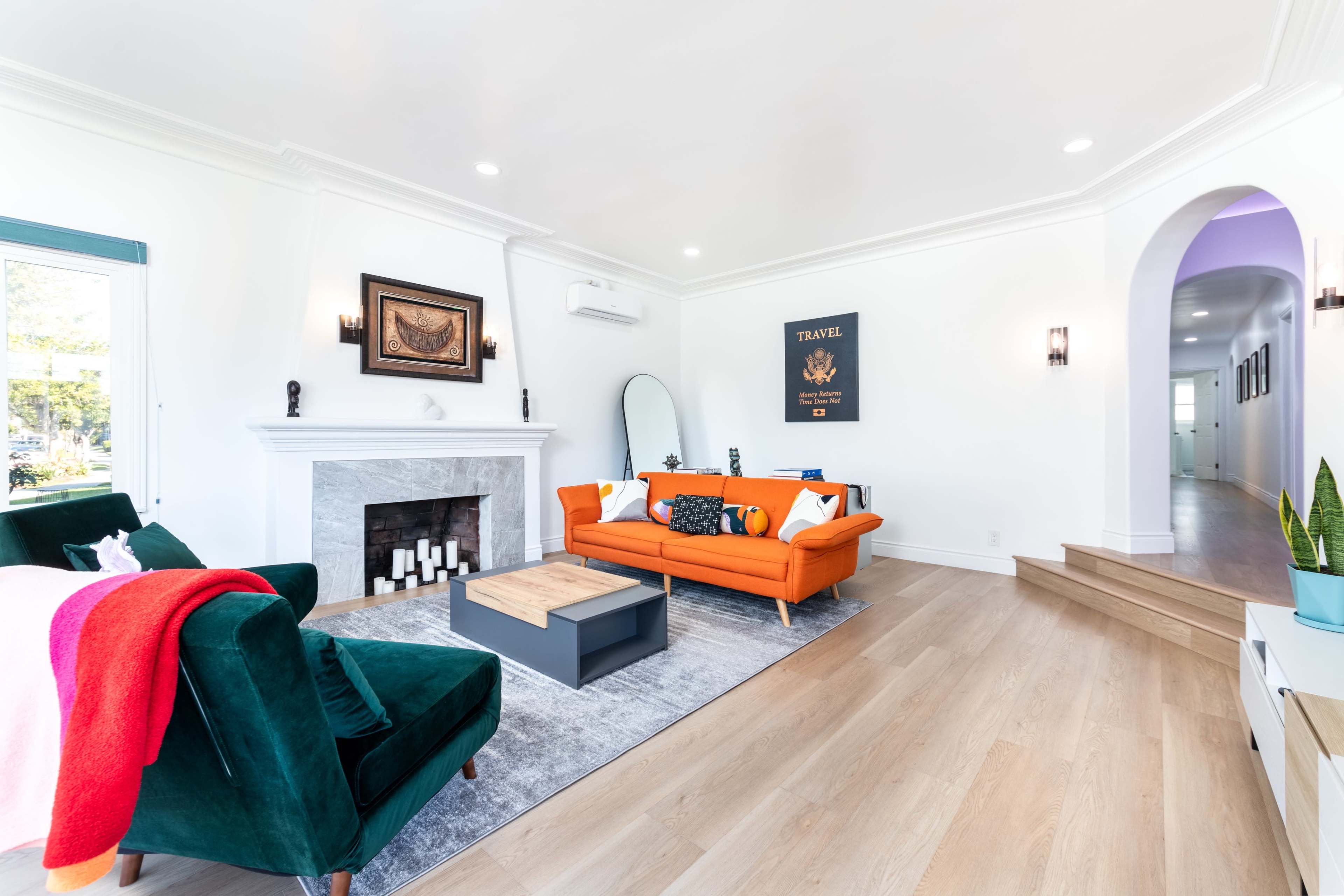 The living room features a white fireplace, an orange sofa, green velvet chairs, and a coffee table on a light wood floor.