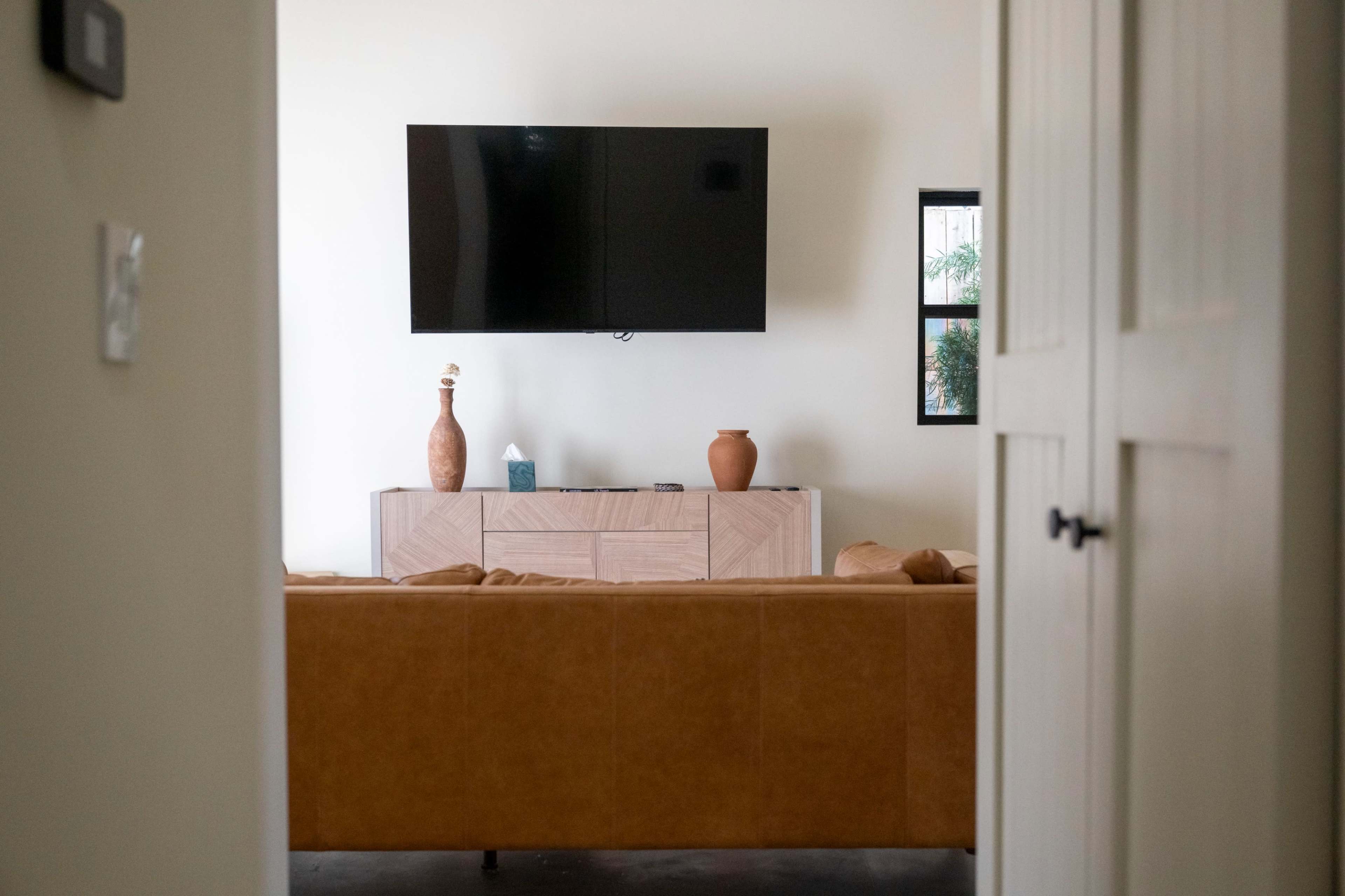 The image shows a living room with a brown couch facing a wooden media console and a wall-mounted television.