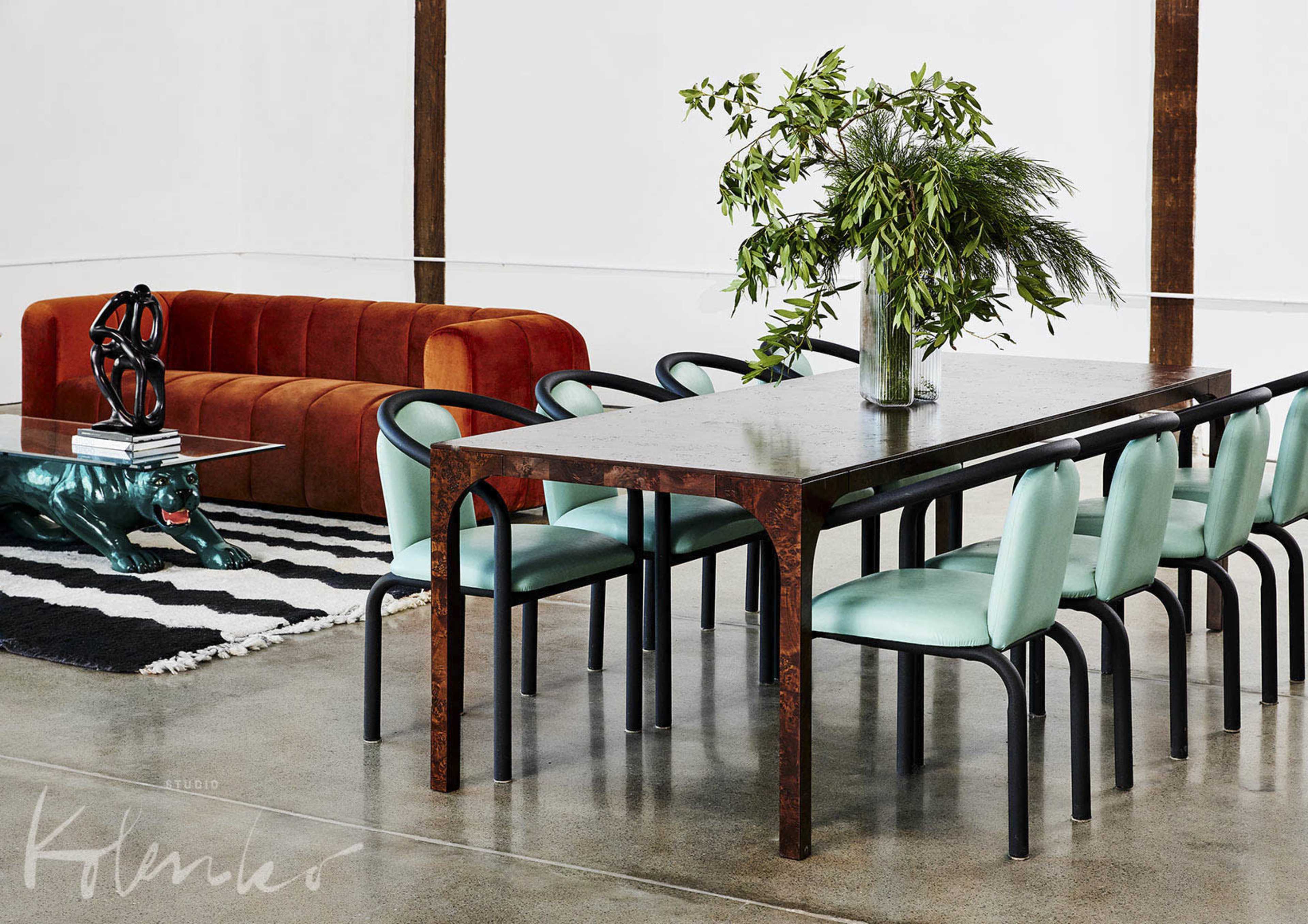A modern living space with a rectangular dining table surrounded by mint green chairs, a red sofa, and a decorative rug on a polished concrete floor.