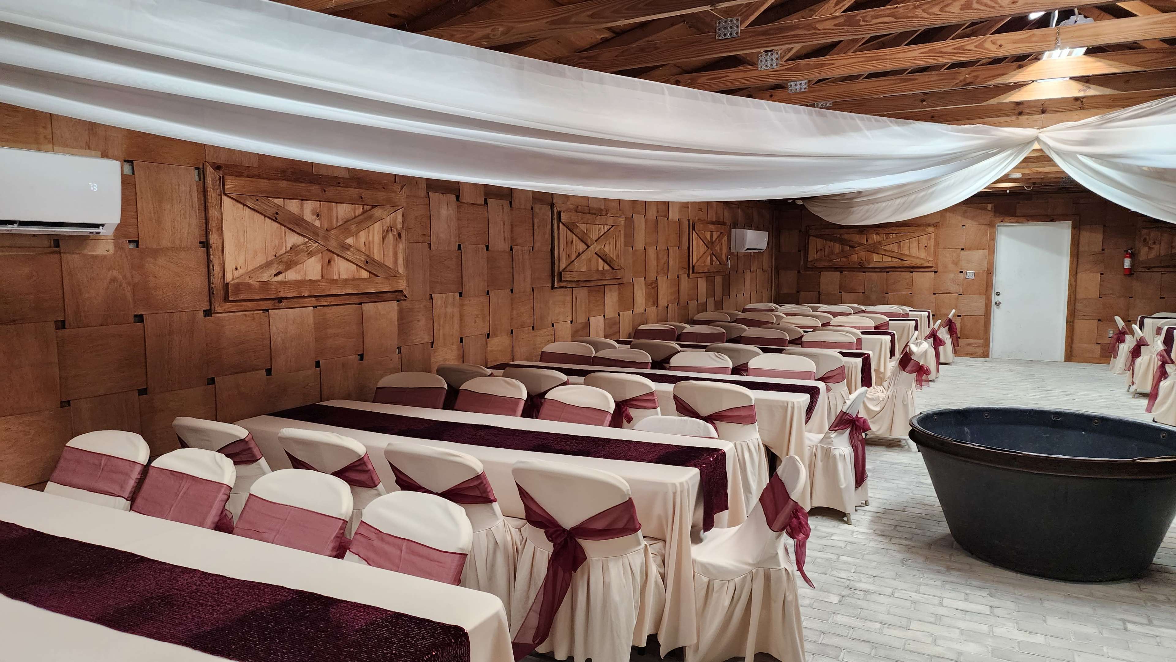 A spacious banquet hall with rows of tables covered in white tablecloths and burgundy runners, surrounded by wooden paneling.