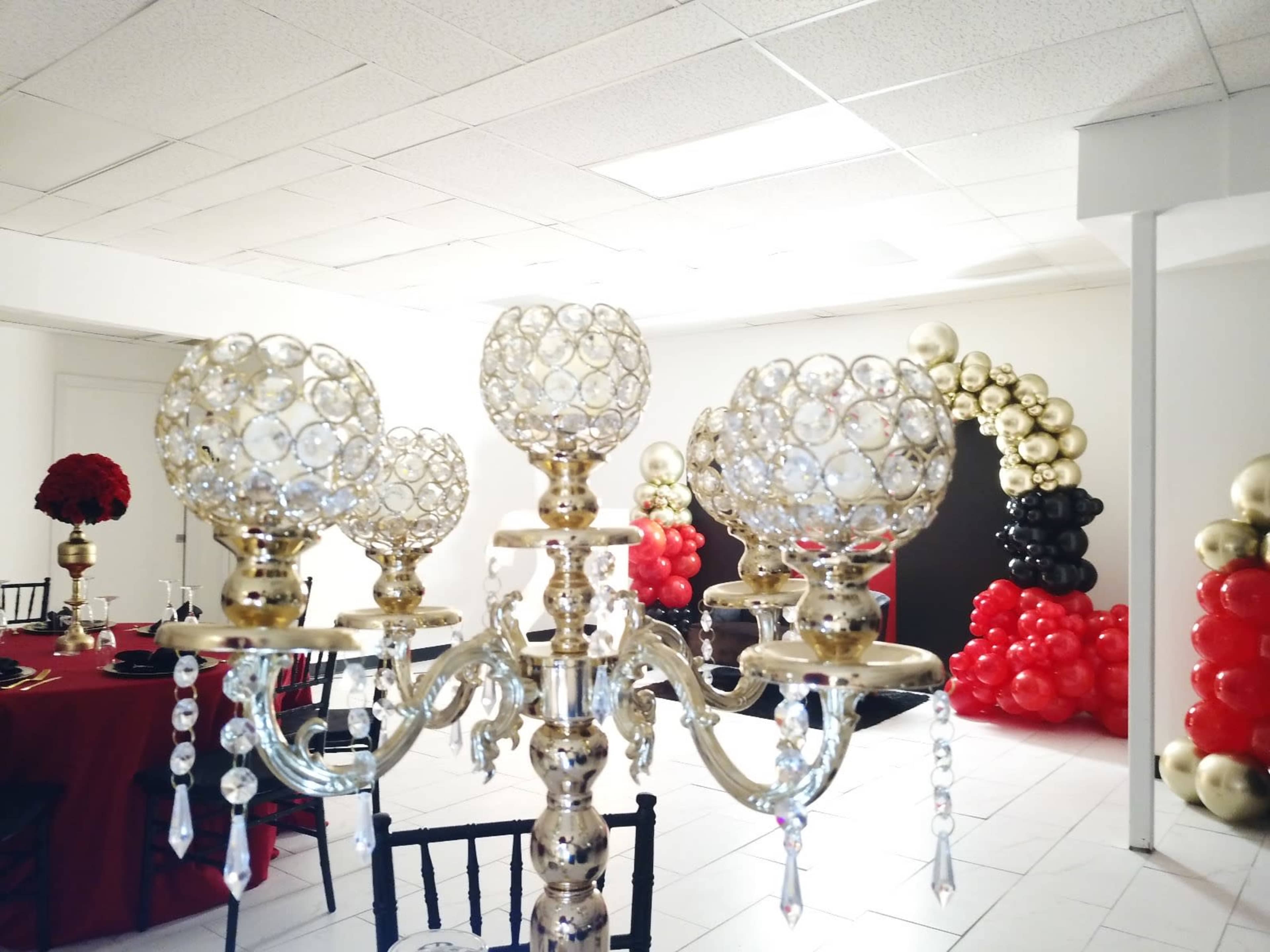 A decorative chandelier with crystal orbs in the foreground, with a backdrop of a party setting featuring red and black balloon archways.