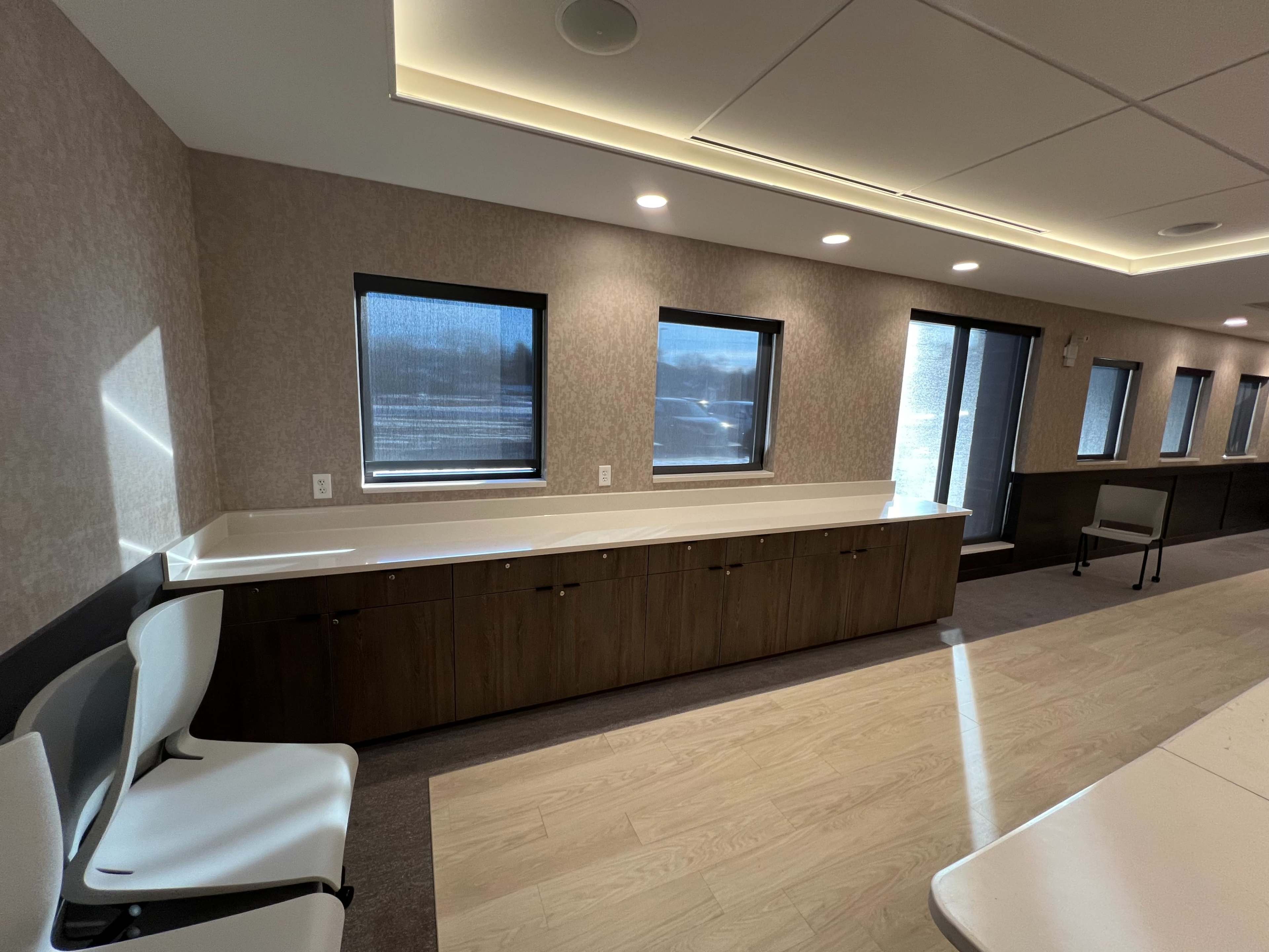 A modern room with two chairs, a long counter with cabinets below, and several windows.