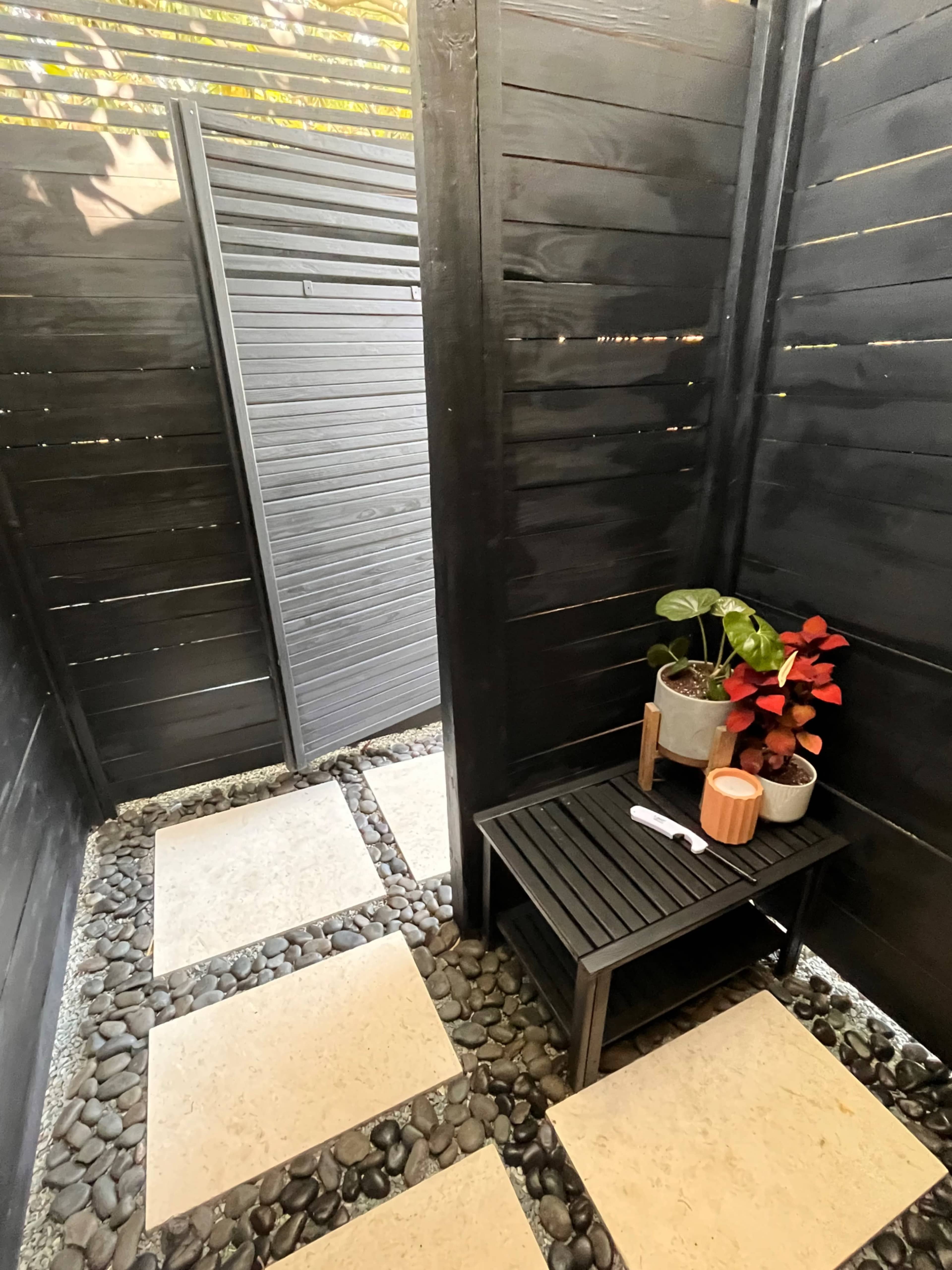 A small, enclosed outdoor space with black wooden slats, a stone pathway, and a table holding potted plants.