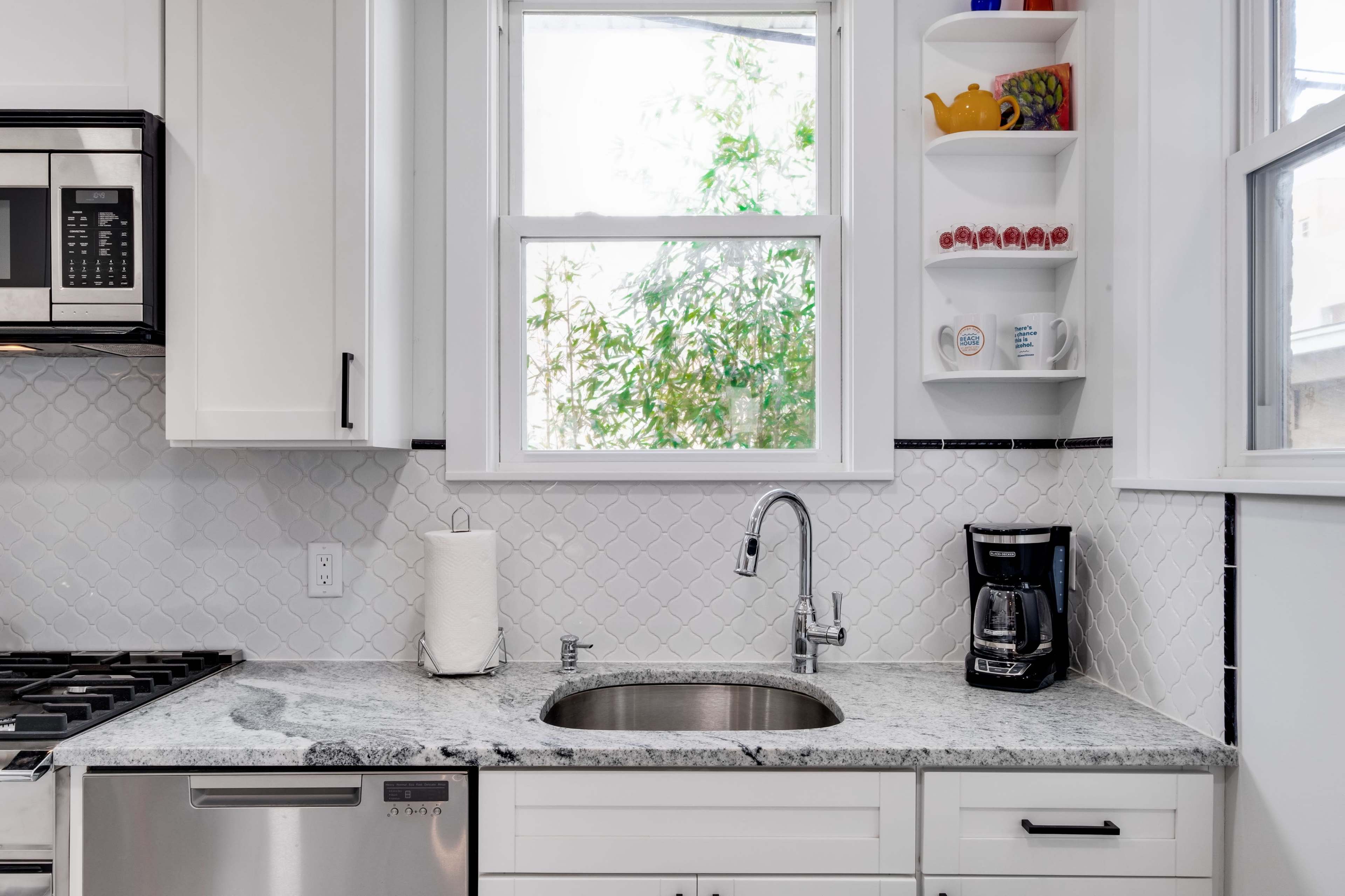 A kitchen countertop with a stainless steel sink, a coffee maker, and a window that overlooks greenery.