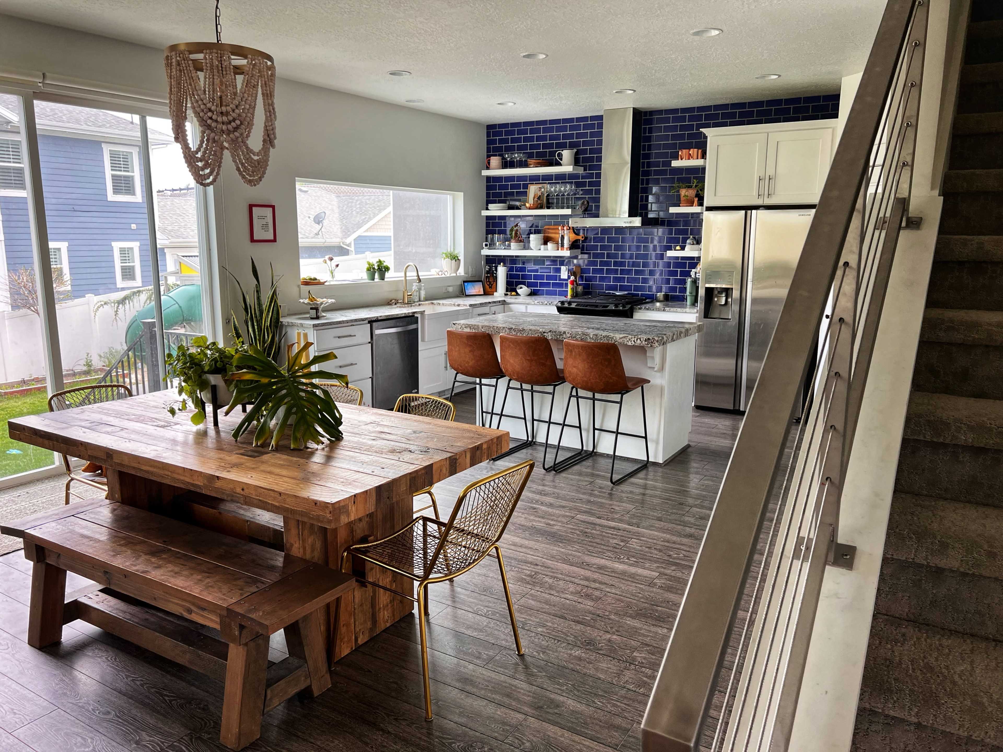 A modern kitchen and dining area with a wooden table, metal chairs, and a blue-tiled backsplash.