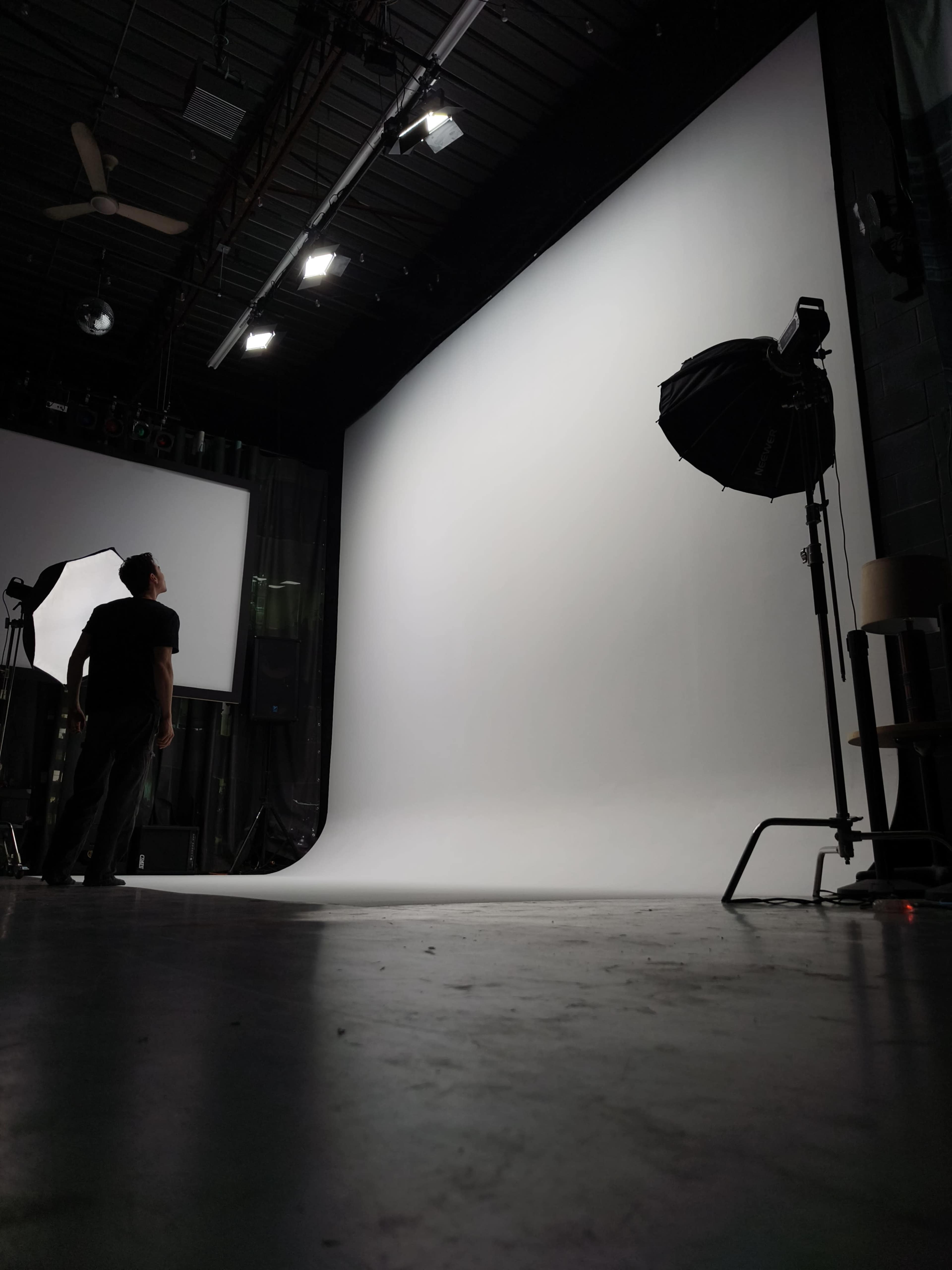 A photographer stands in a studio with a blank backdrop and studio lights arranged for a photoshoot.