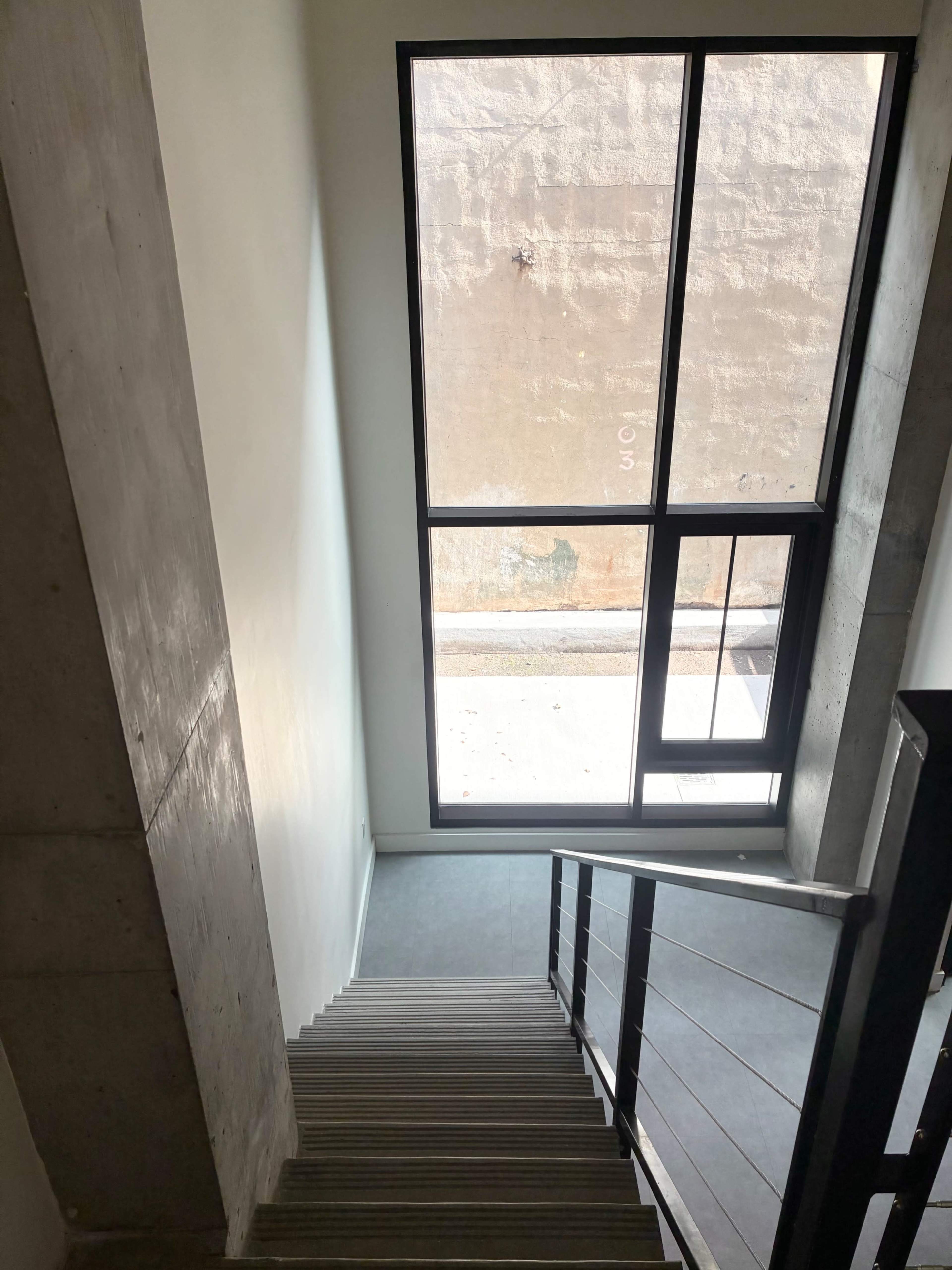 A staircase leads down to a large window overlooking a concrete wall outside.