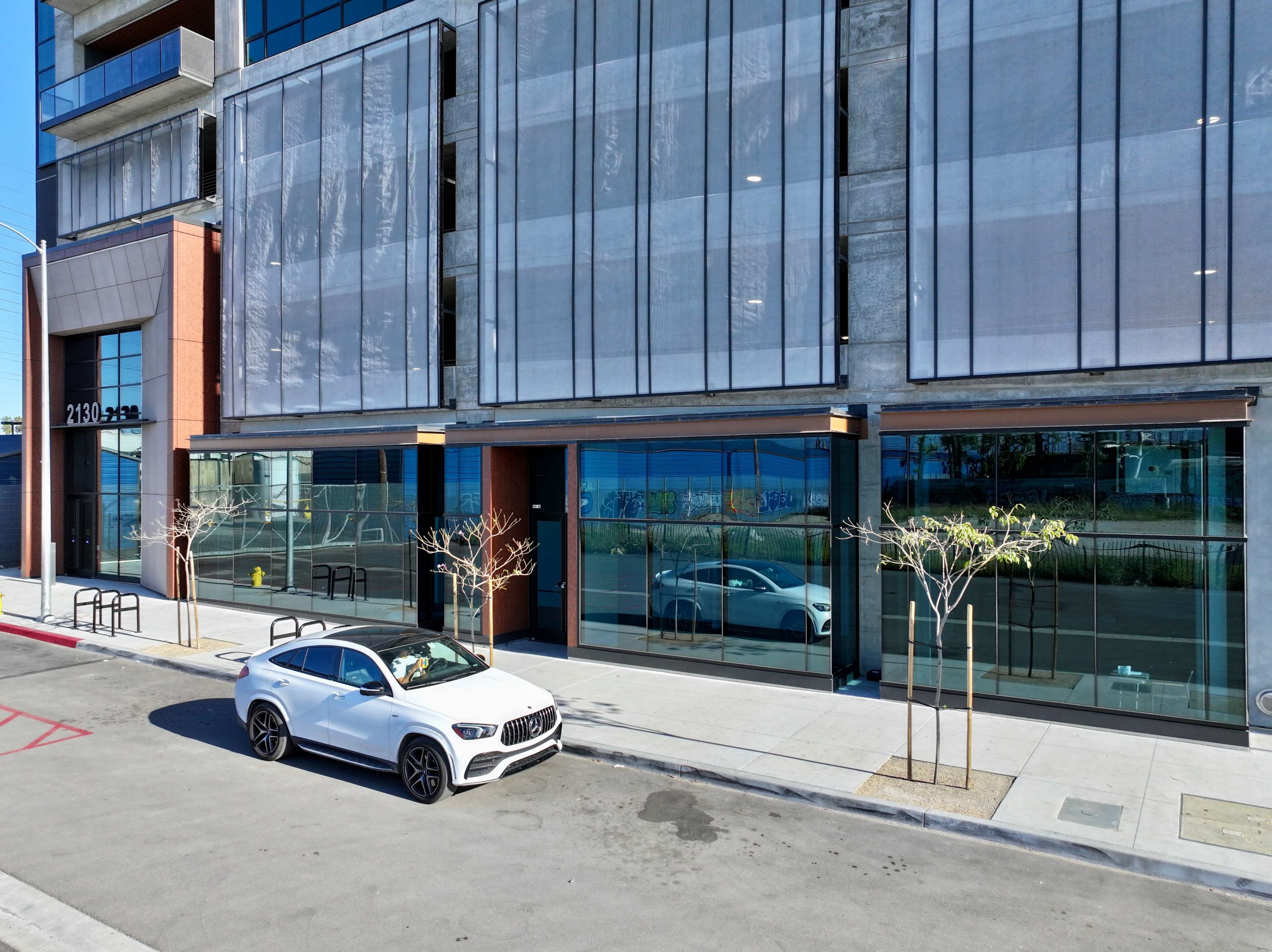 A white car is parked in front of a modern building with large windows and a concrete facade.