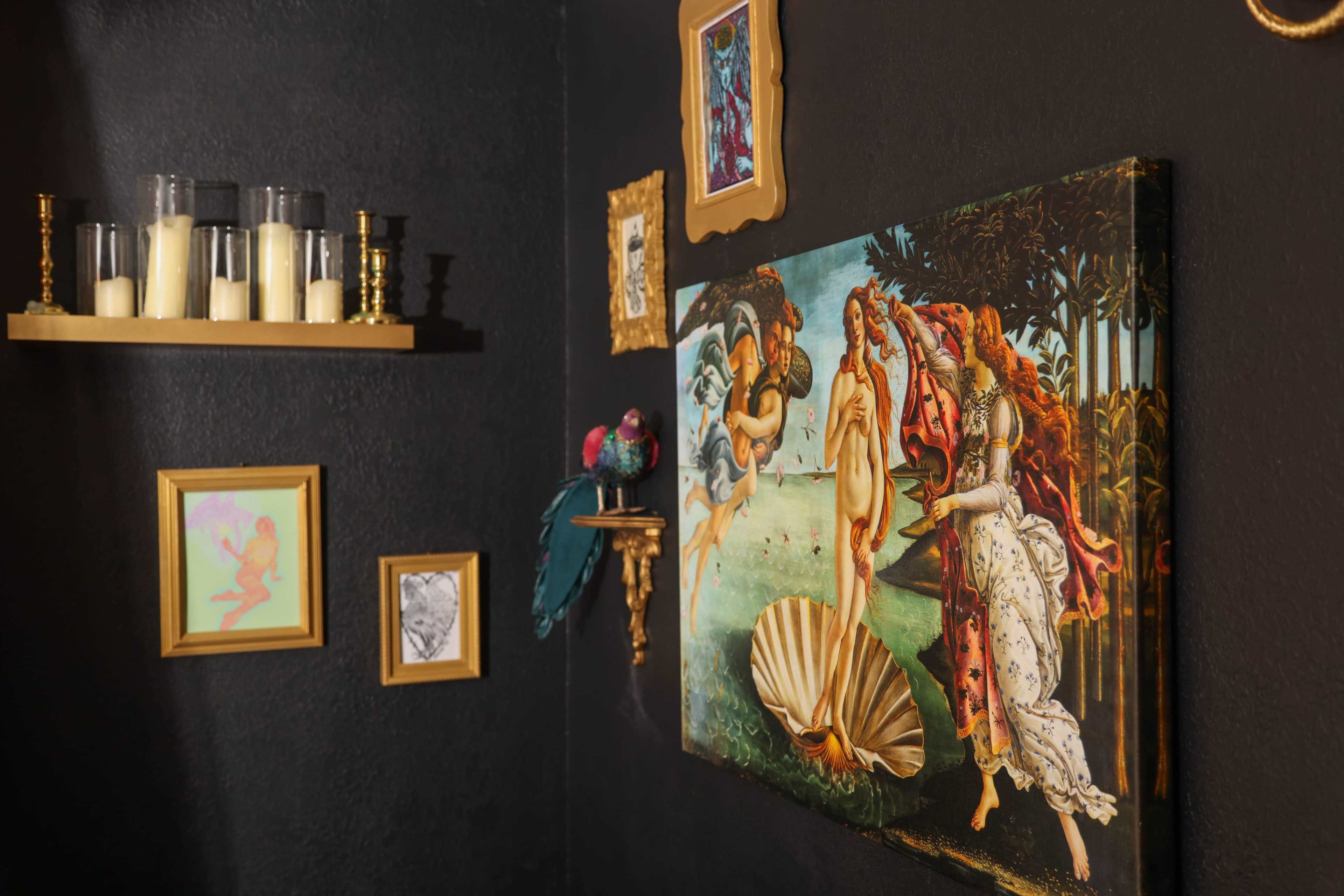 The image shows a black wall featuring an assortment of framed art, a painting of a classical scene, and decorative items on shelves.