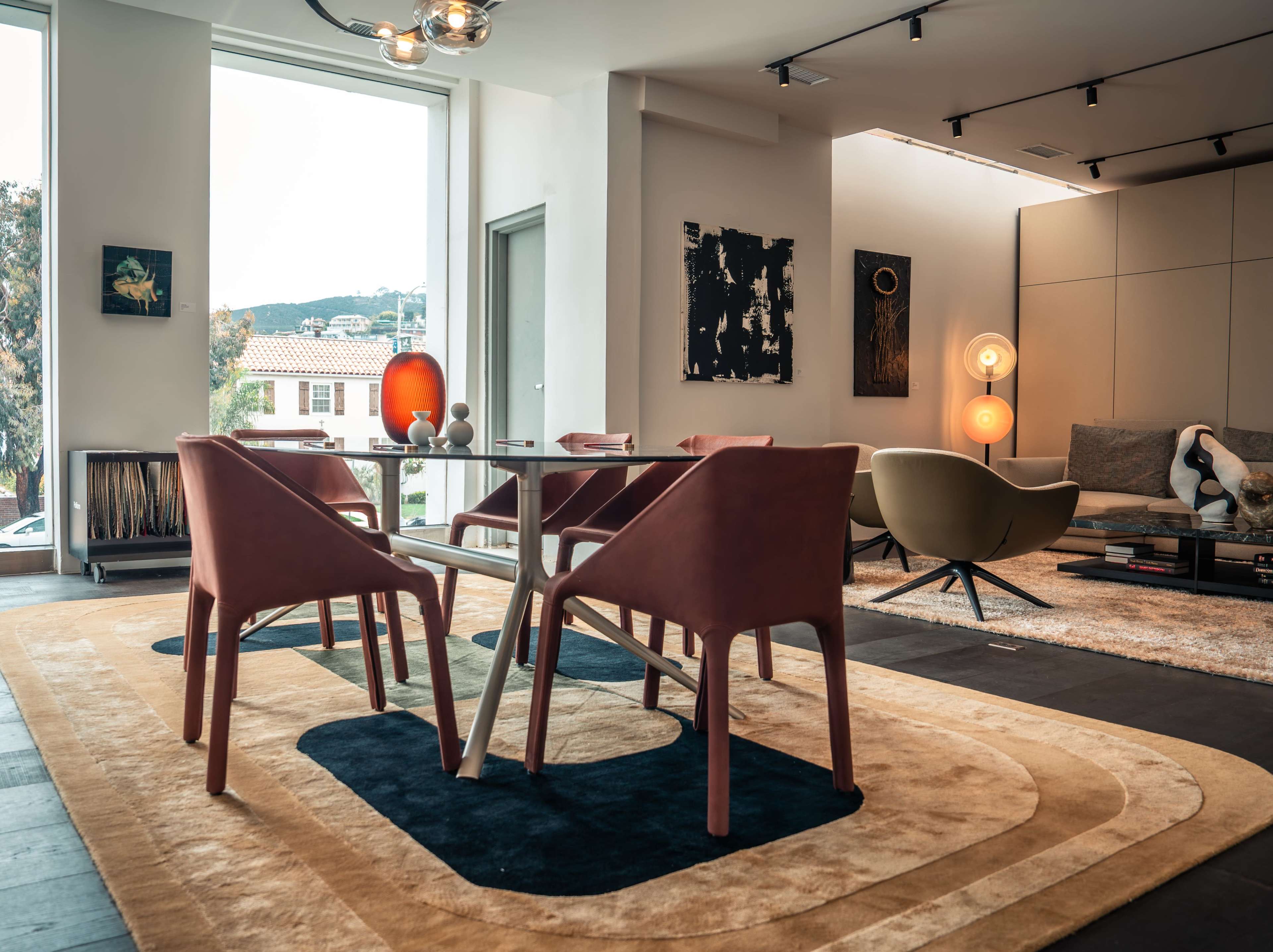 The image depicts a modern living space featuring a glass dining table surrounded by four chairs, an accent chair, and various artwork on the walls.