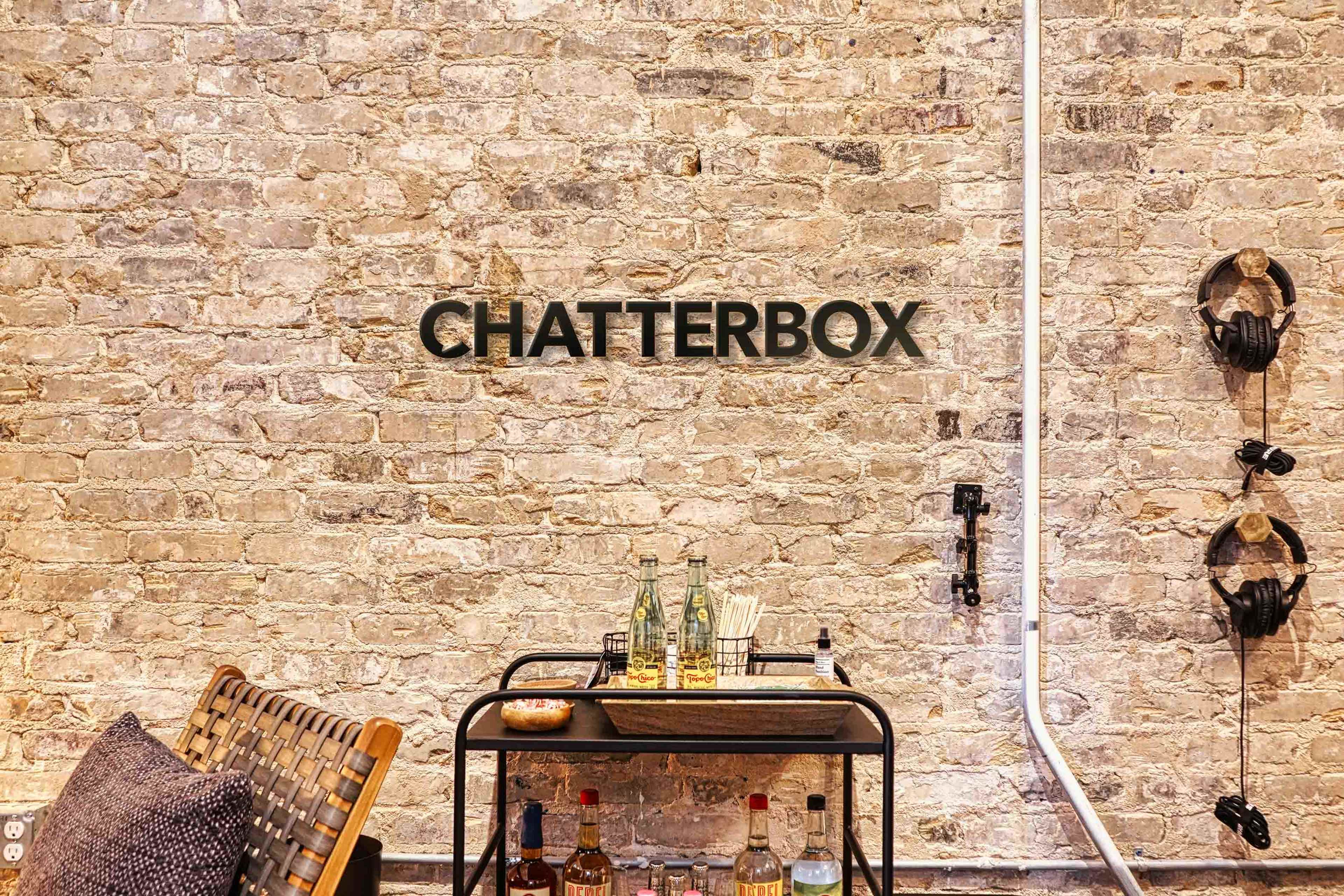 A rustic brick wall with the word "CHATTERBOX" displayed prominently, alongside a wooden cart holding various bottles and glasses.