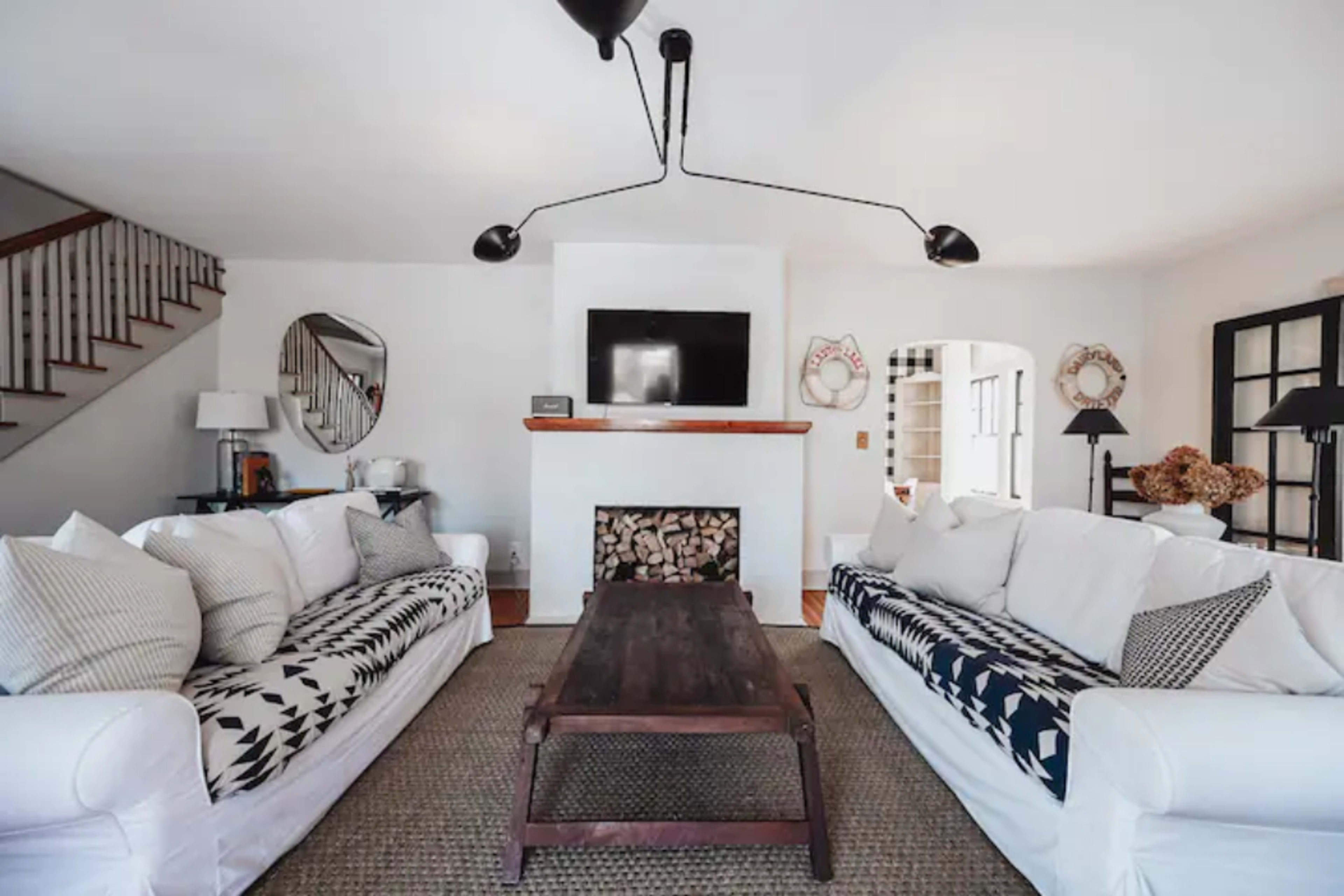 The living room features two large sofas arranged around a central wooden coffee table, with a fireplace and television mounted on the wall behind them.