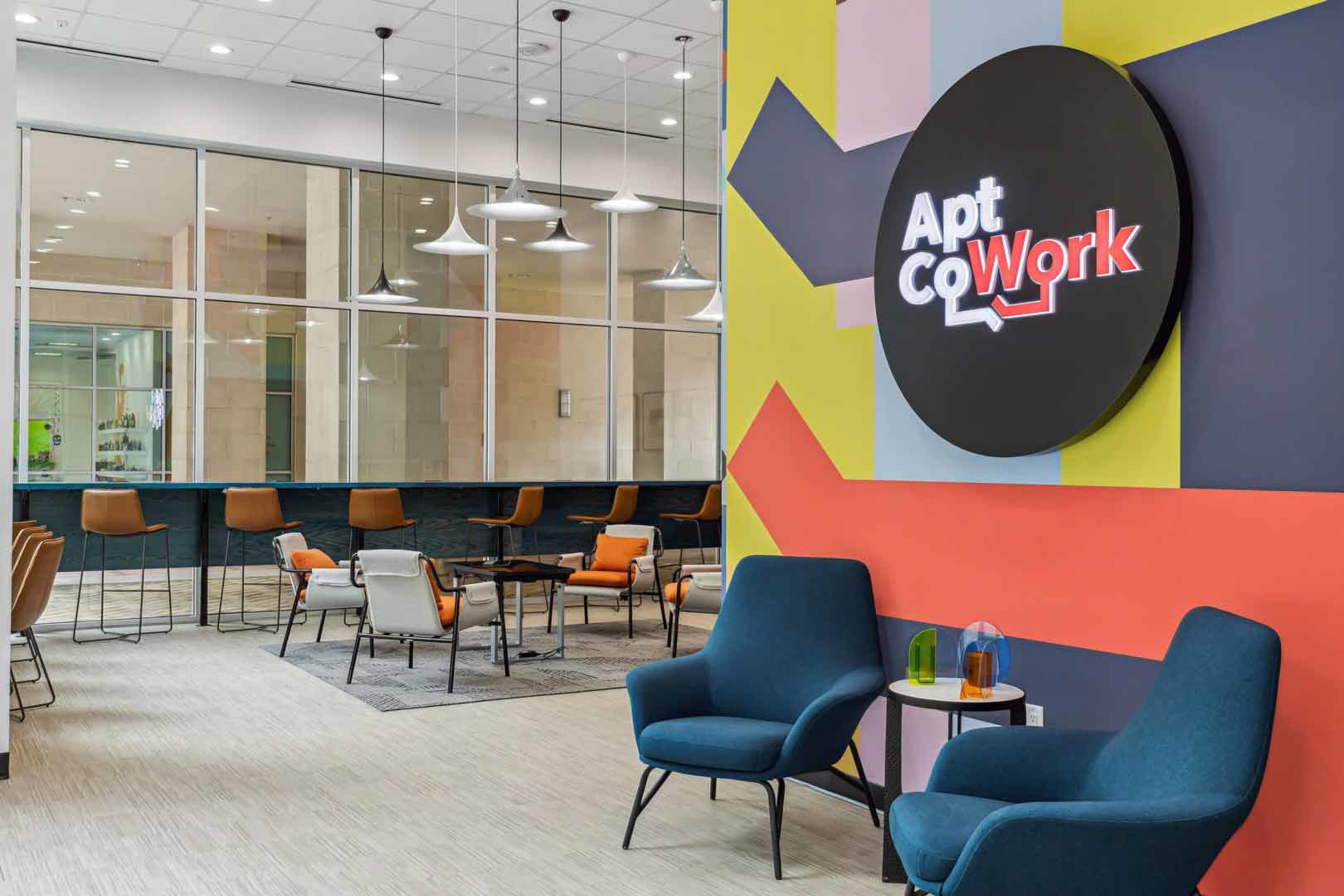 A modern co-working space featuring colorful walls, sleek furniture, and a sign that reads "Apt CoWork."