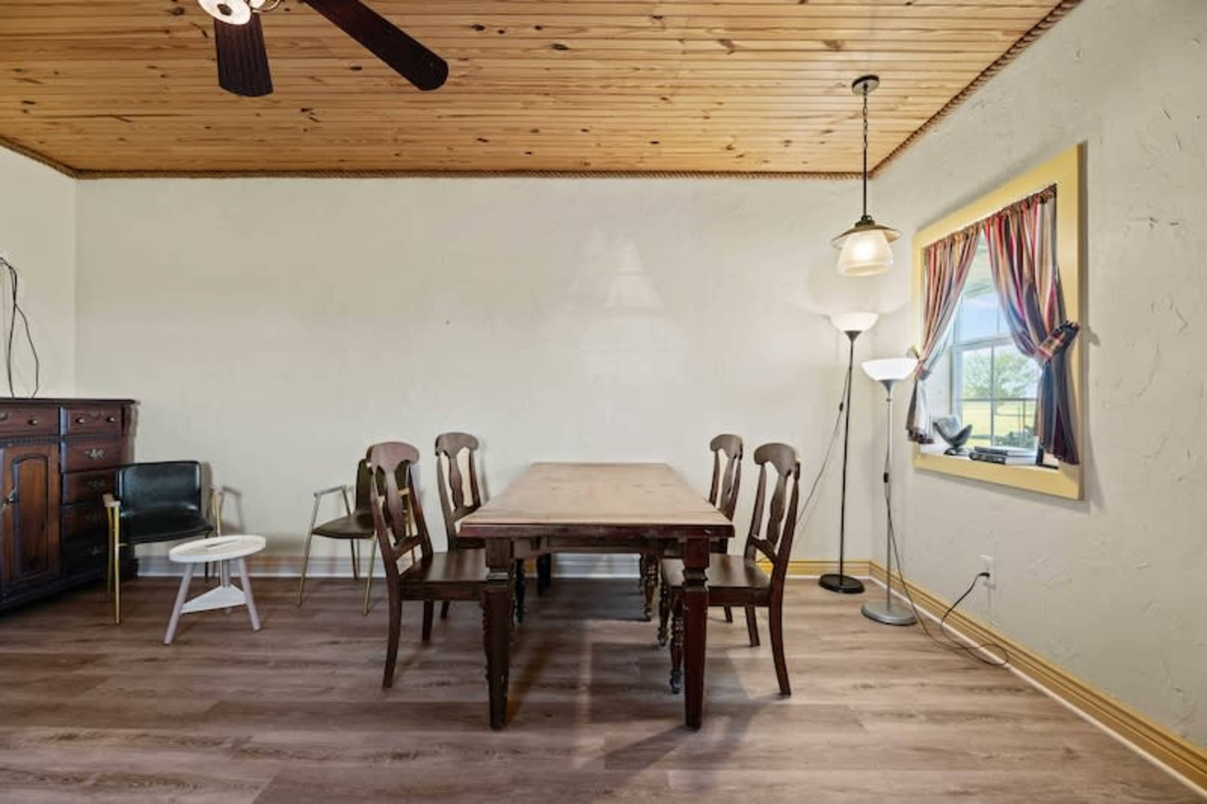 A dining area with a wooden table surrounded by five chairs, a floor lamp, and a cabinet against the wall, all set beneath a wooden ceiling.