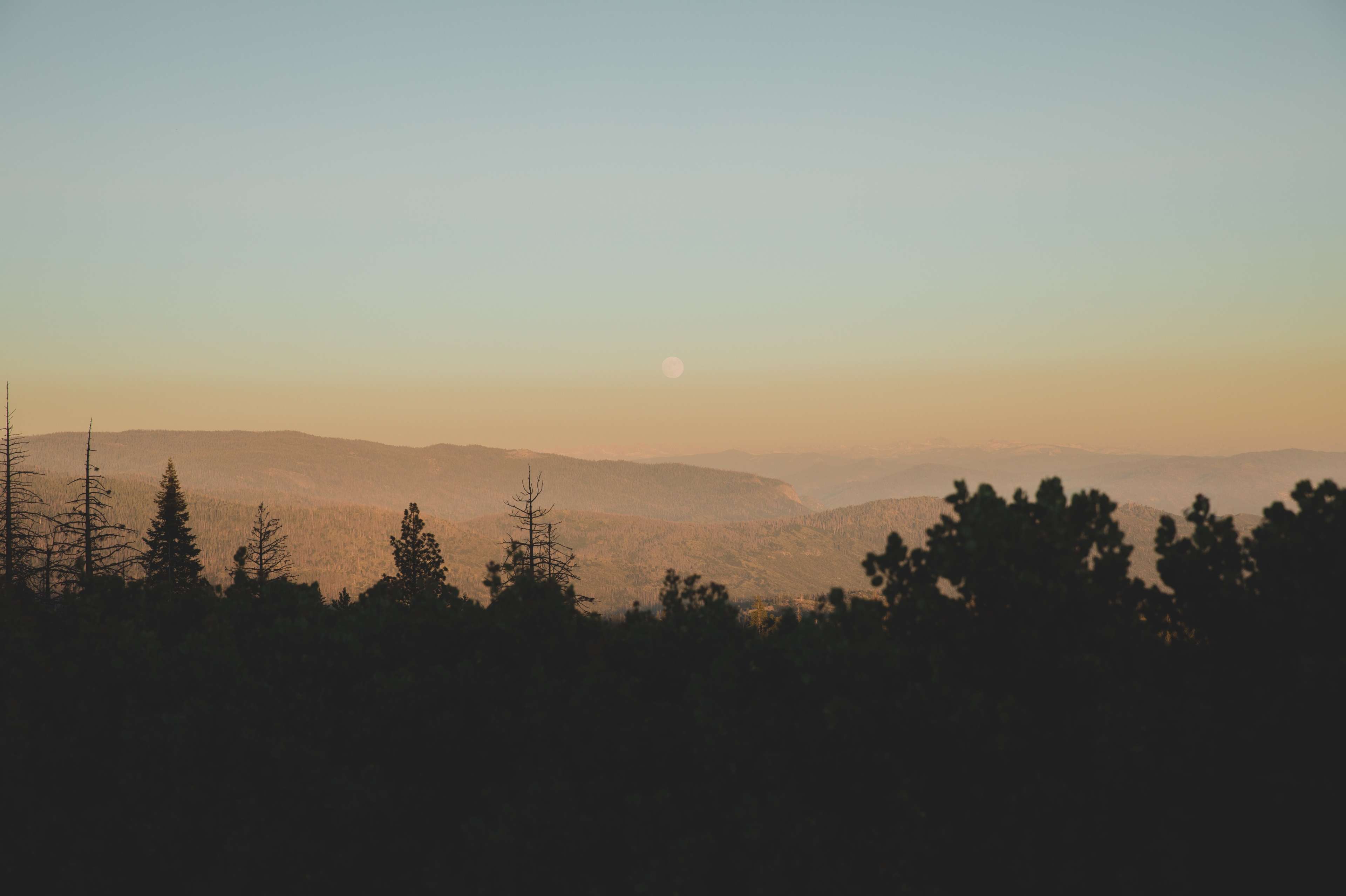 A landscape with distant mountains and a rising moon against a gradient sky at dusk.