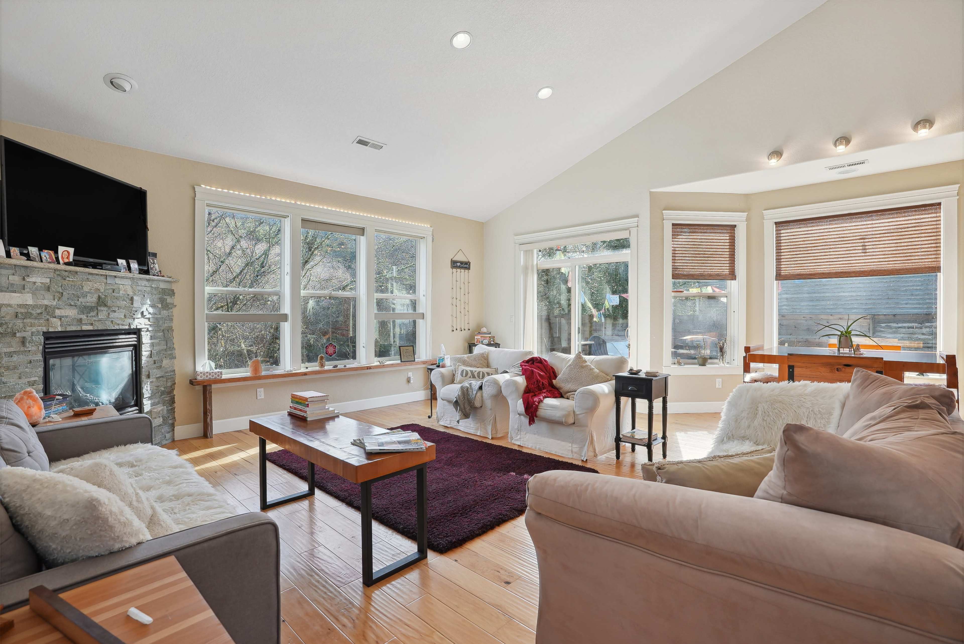 The living room features large windows that provide natural light, a stone fireplace, and a mixture of seating options including sofas and armchairs.