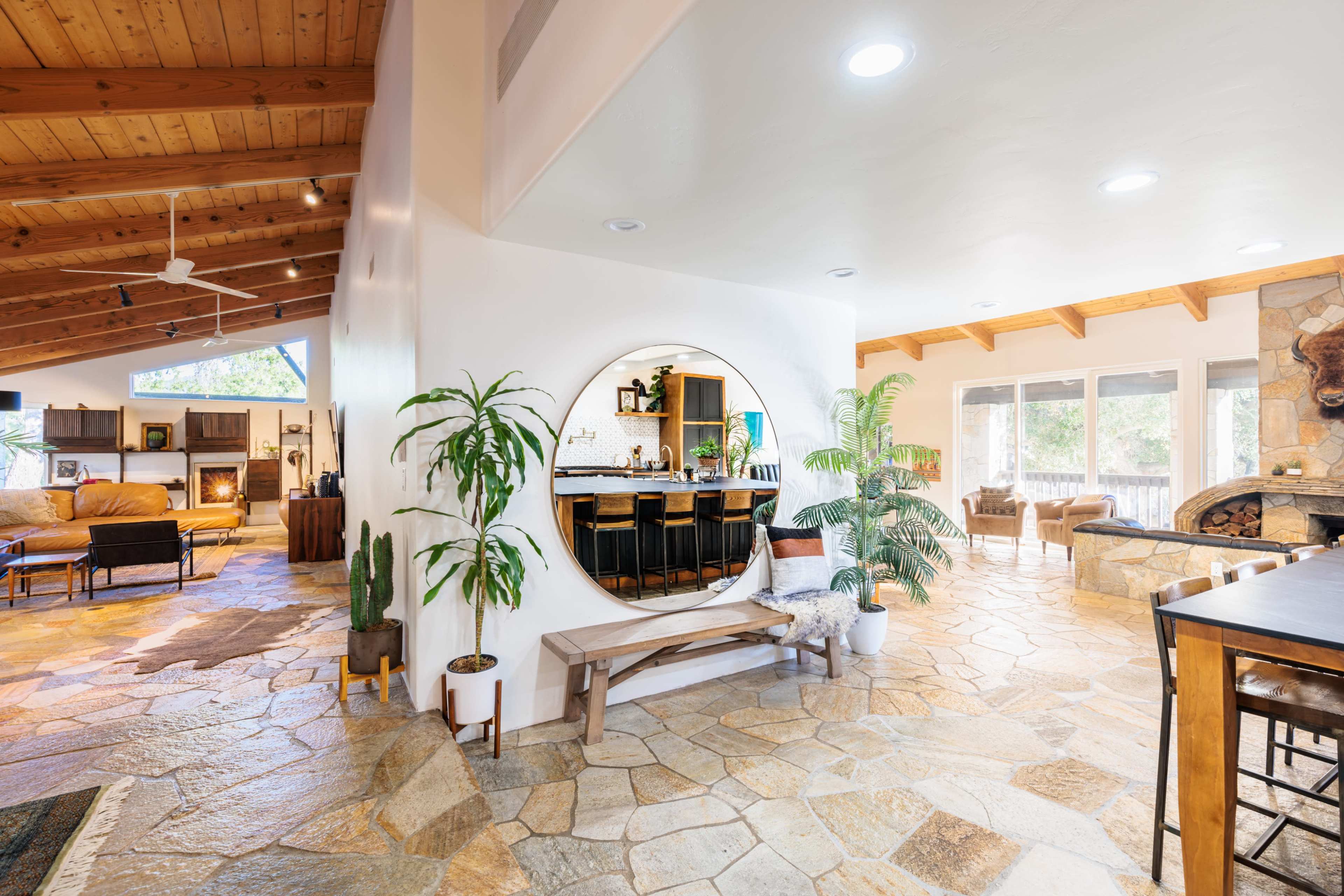 A spacious, open-concept living area with stone flooring, a circular mirror feature, and a cozy seating arrangement next to a fireplace.