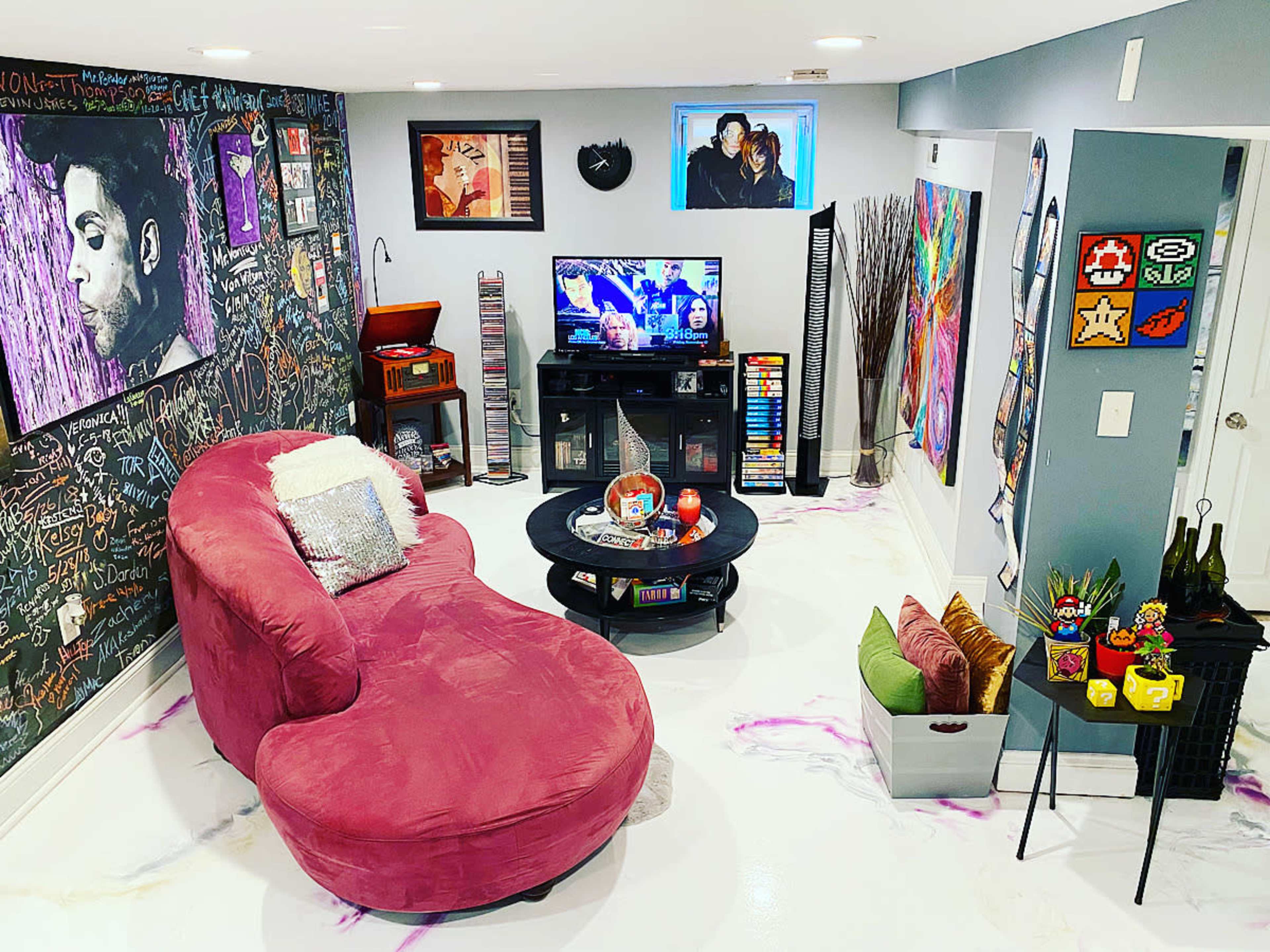 A creatively decorated basement lounge features a large pink couch, a television, and walls covered in colorful artwork and chalk drawings.