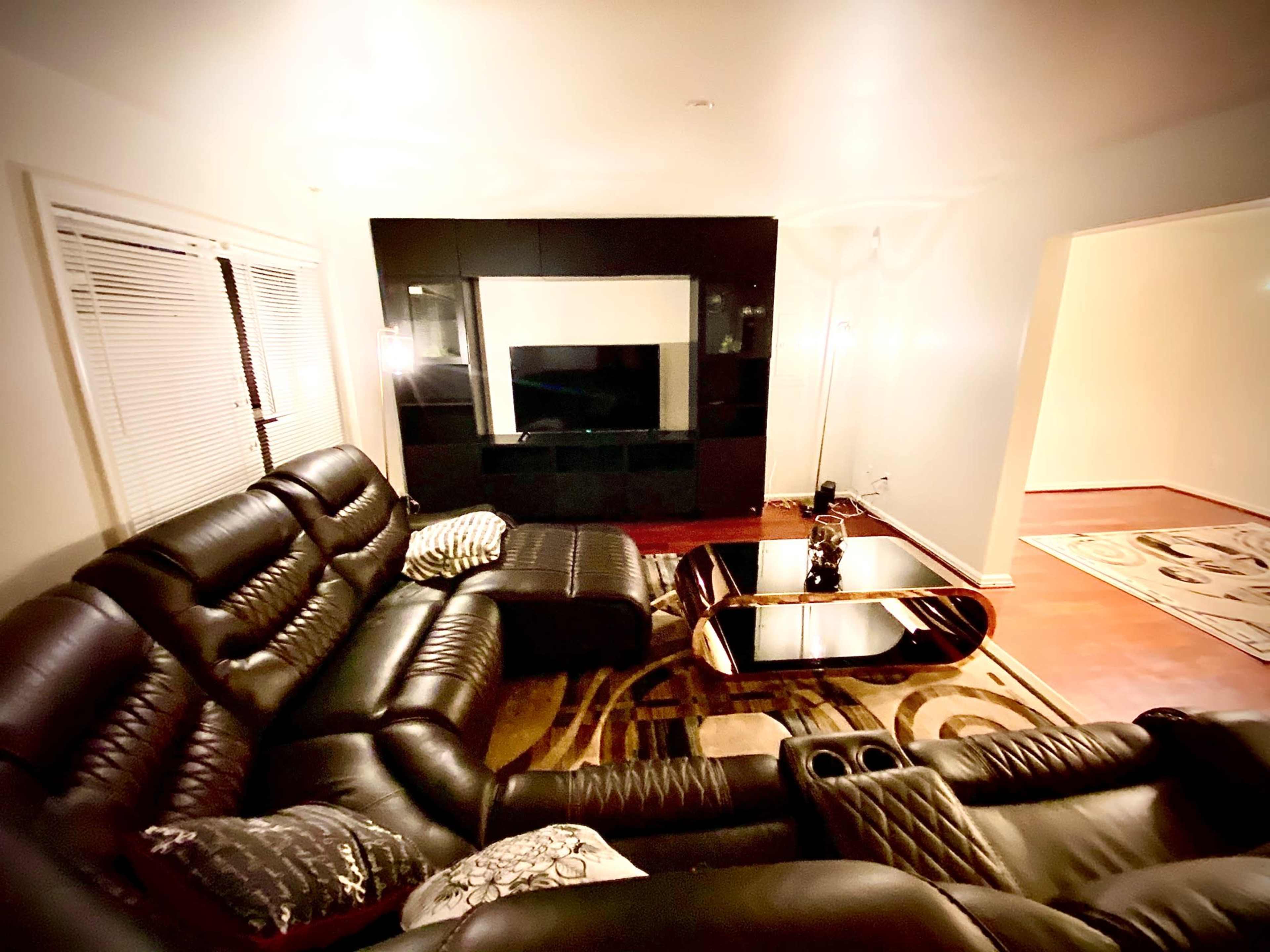 A modern living room featuring black leather furniture, a glass coffee table, and a wall-mounted television.