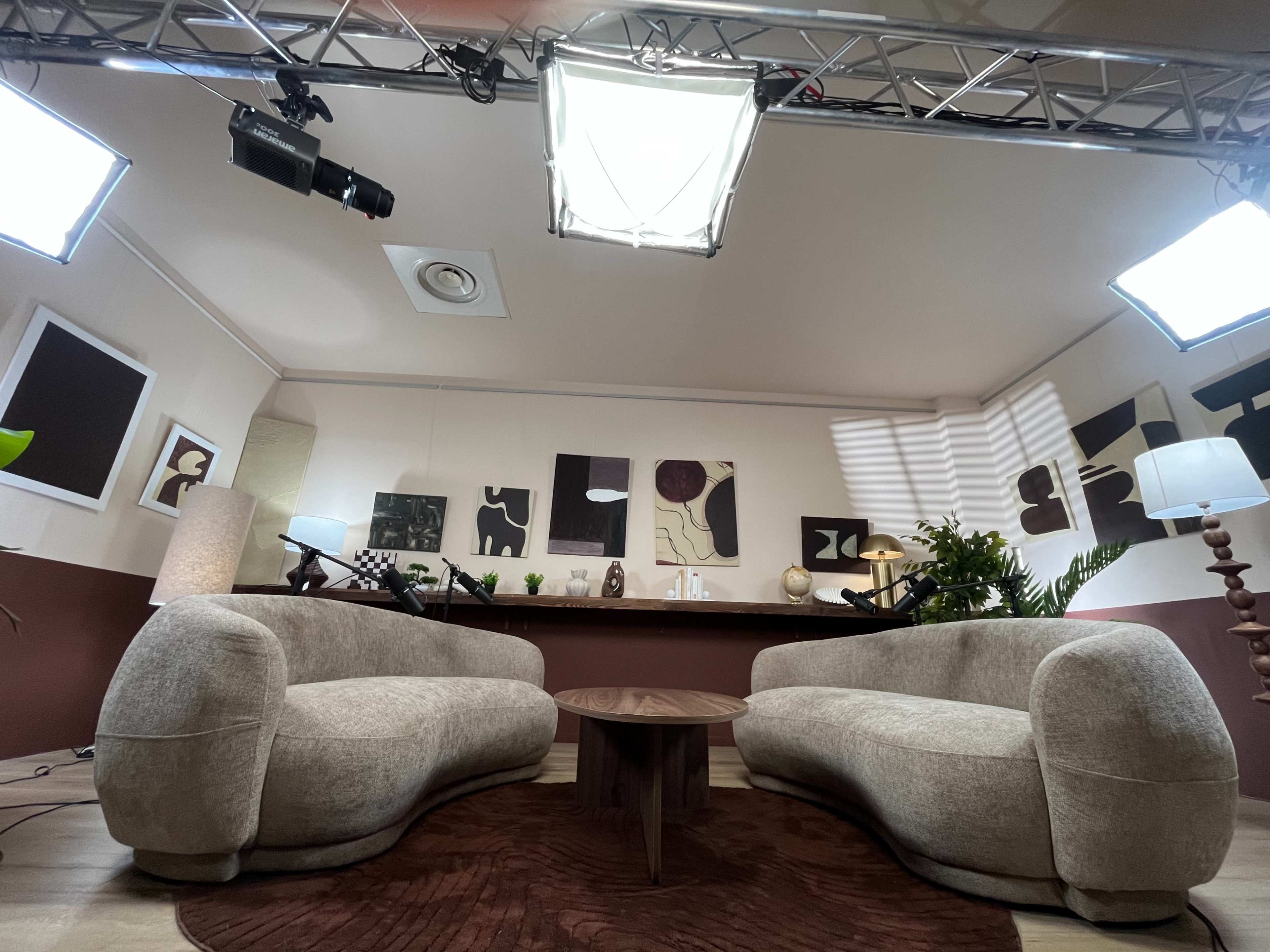The image shows a modern studio setup with two curved sofas facing a small table, surrounded by artworks and soft lighting.
